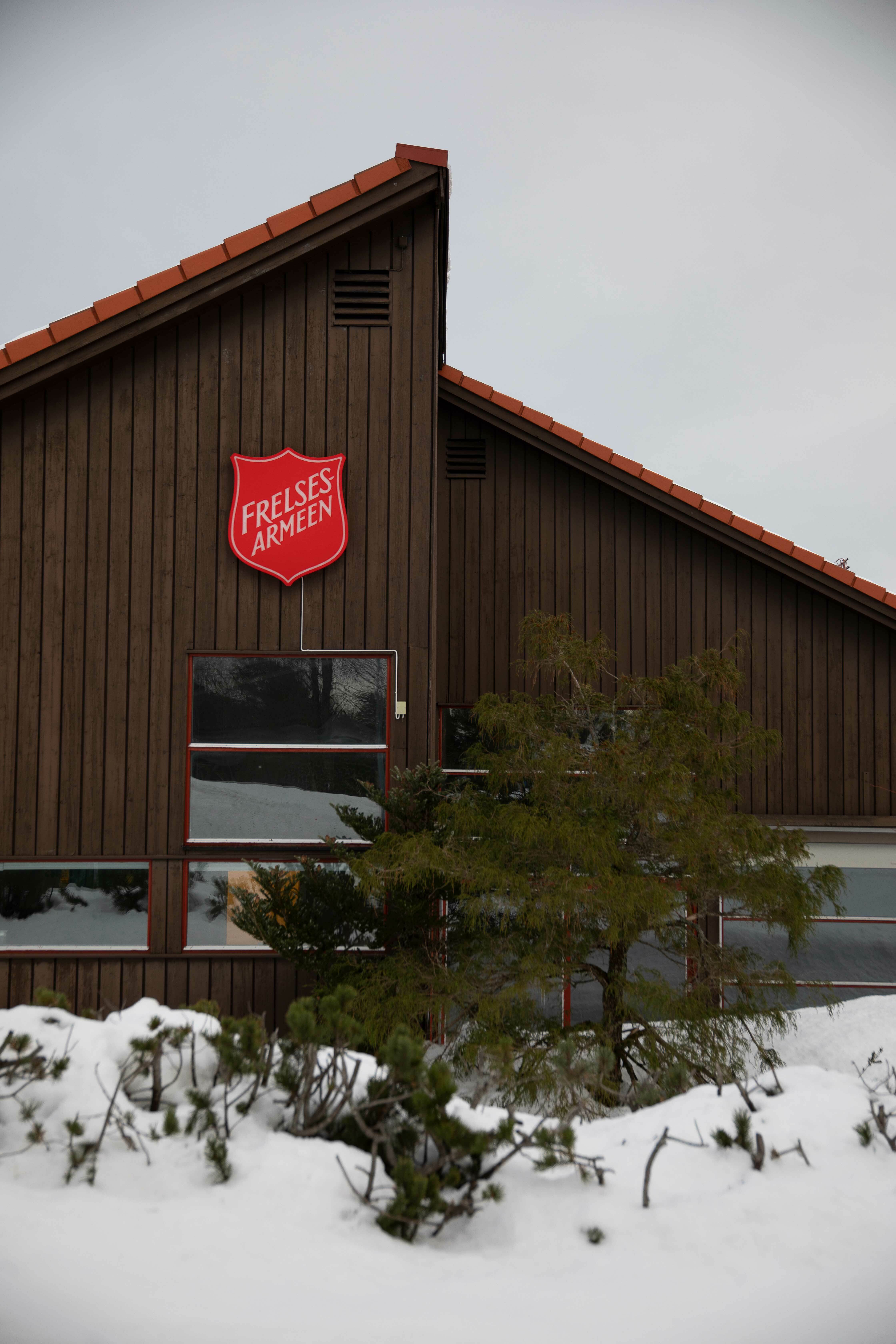 Bilde av et moderne, brunt trebygg med Frelsesarmeens logo på. Ute er det snø.