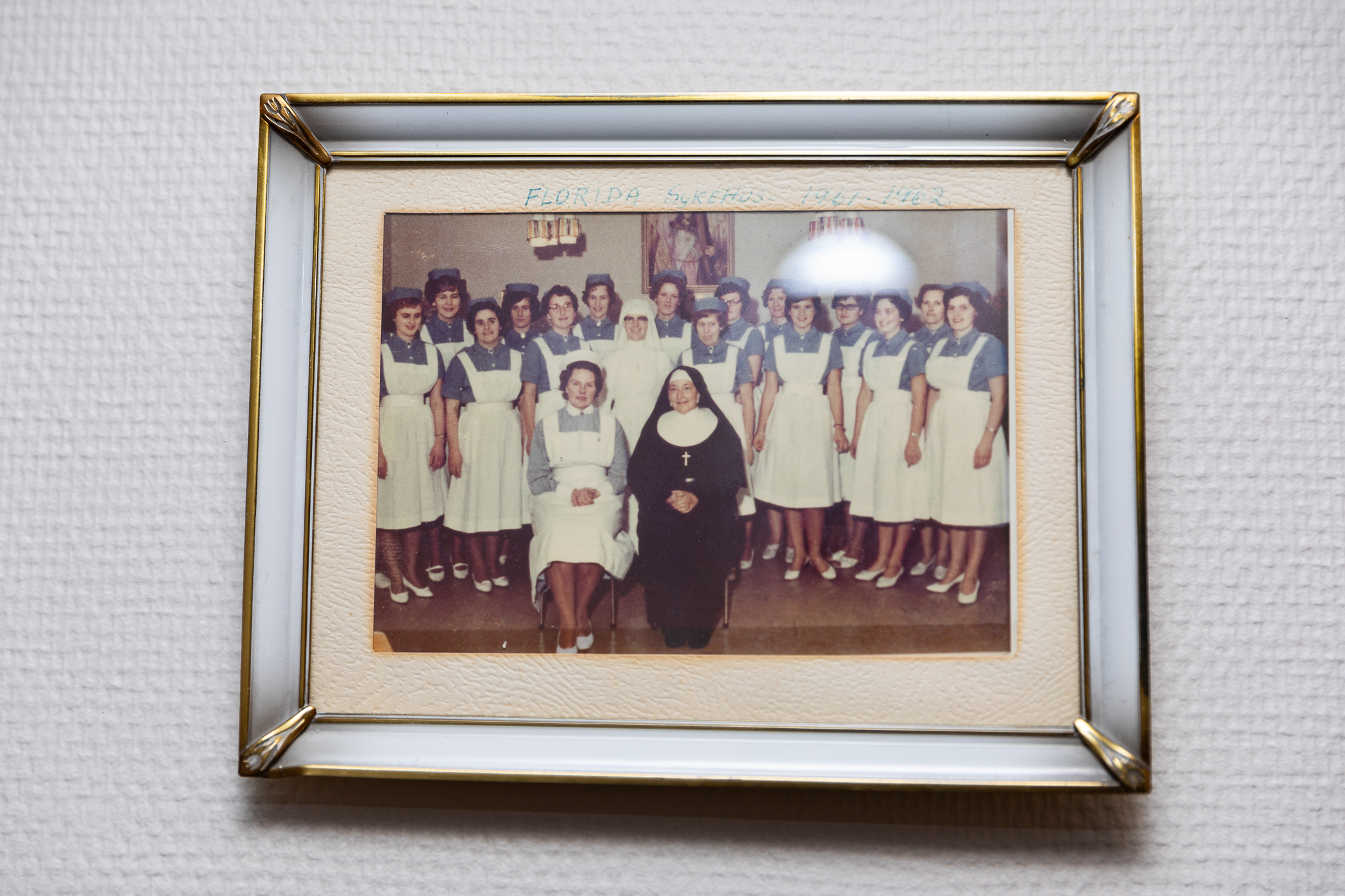 Et eldre bilde i ramme som viser et kull sykepleiere. Alle er kvinner og en nonne kledt i sort og hvitt sitter på første rekke.