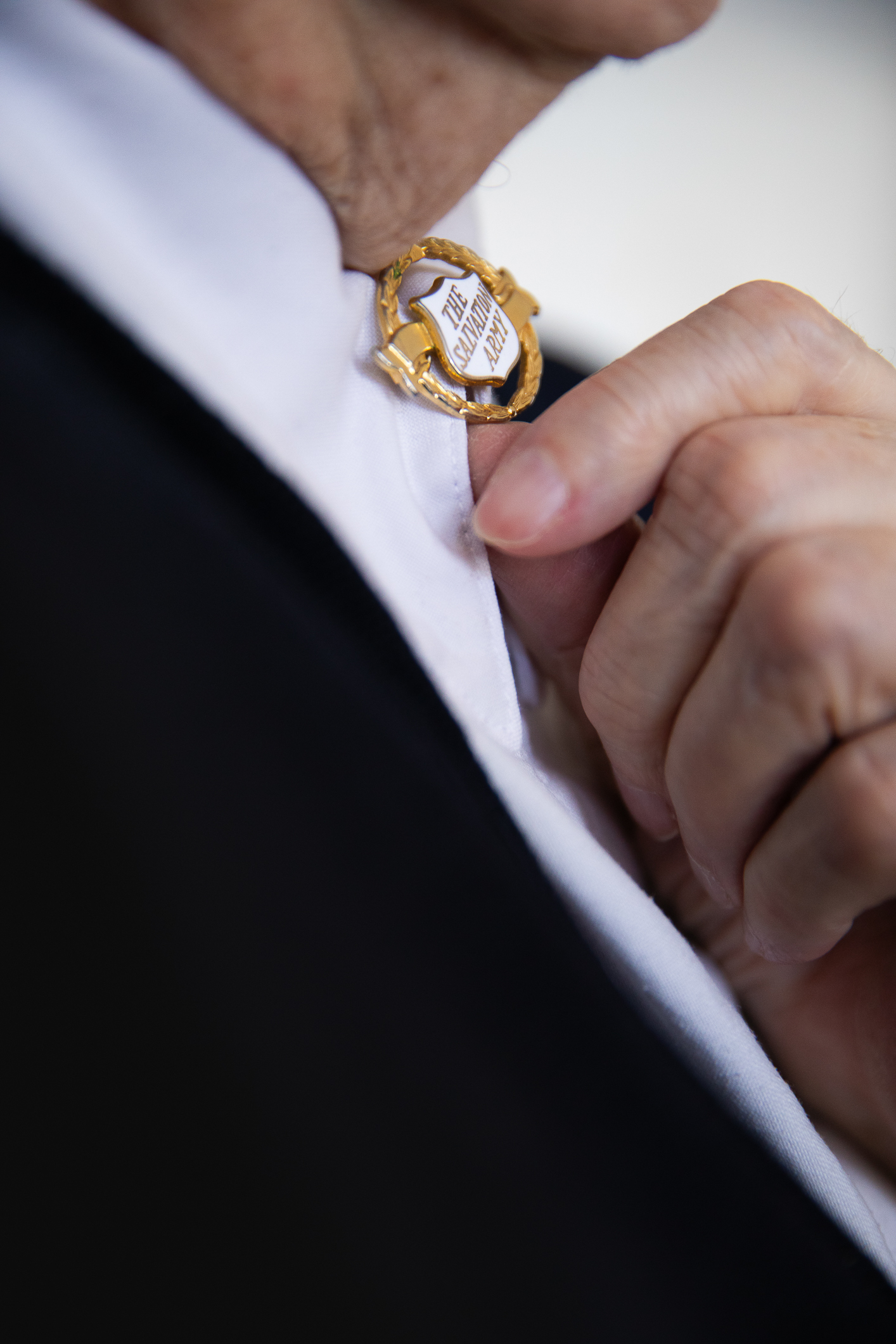 Endre kvinne viser fram en gullnål som hun har i halskragen. Hun har hvit bluse og mørk jakke.