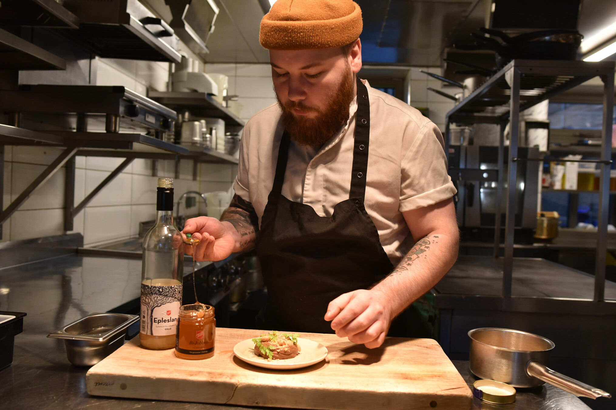 Foto: Kokken tar en skje med honning opp fra en krukke. Foran ham står en tallerken med en matrett anrettet.