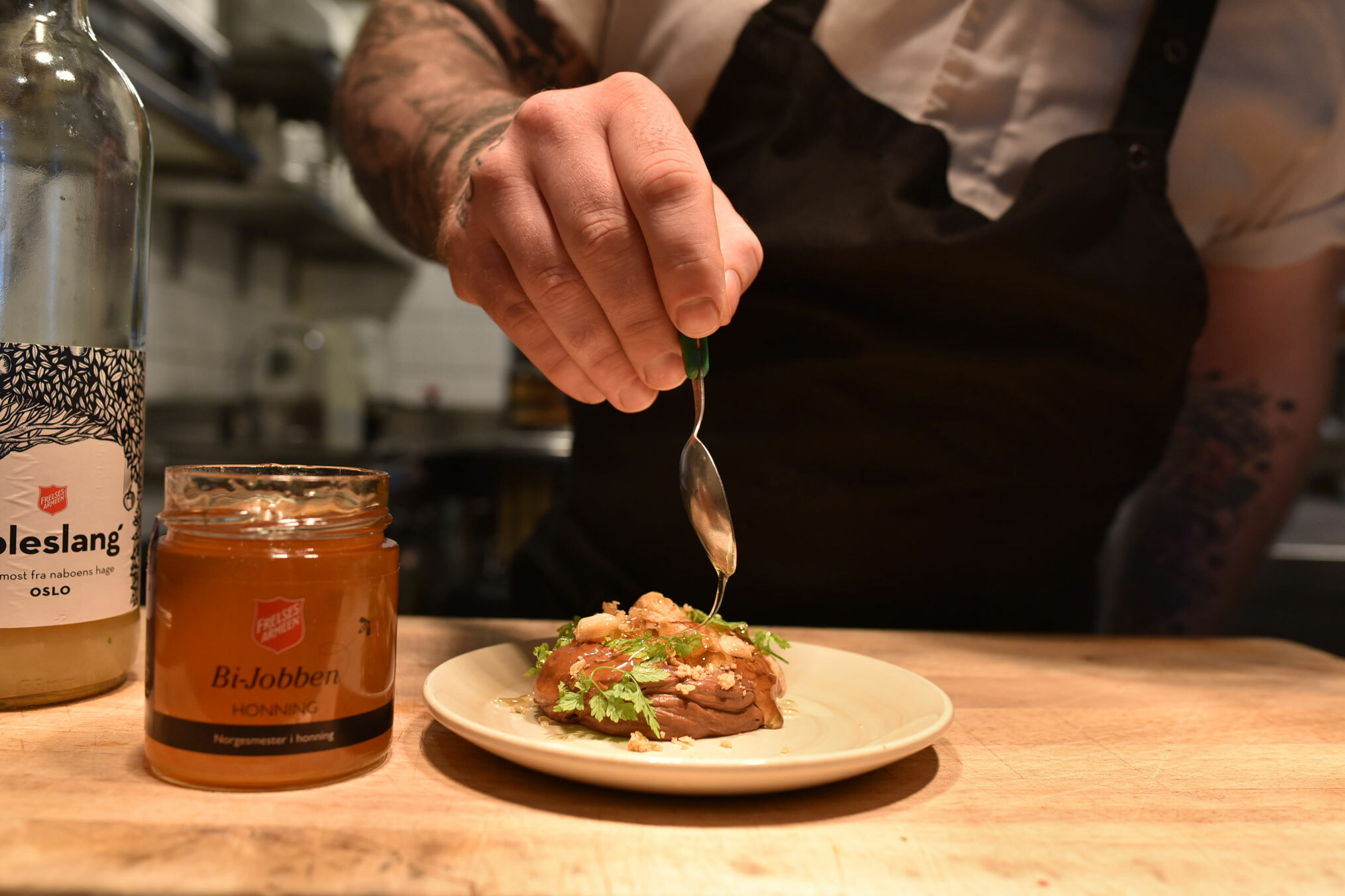 Foto: Hånd som sprer litt honning med en skje utover en rett dandert på tallerkenen.