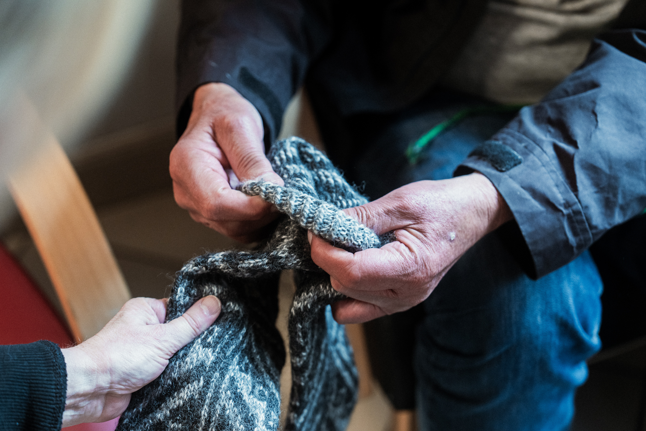 En kvinnehånd som gir et par strikkede ullsokker i blått og grått med avansert mønster og en mann med grove hender som kjenner på dem. Vi ser et bildeutsnitt, så vi ser ikke hodene.