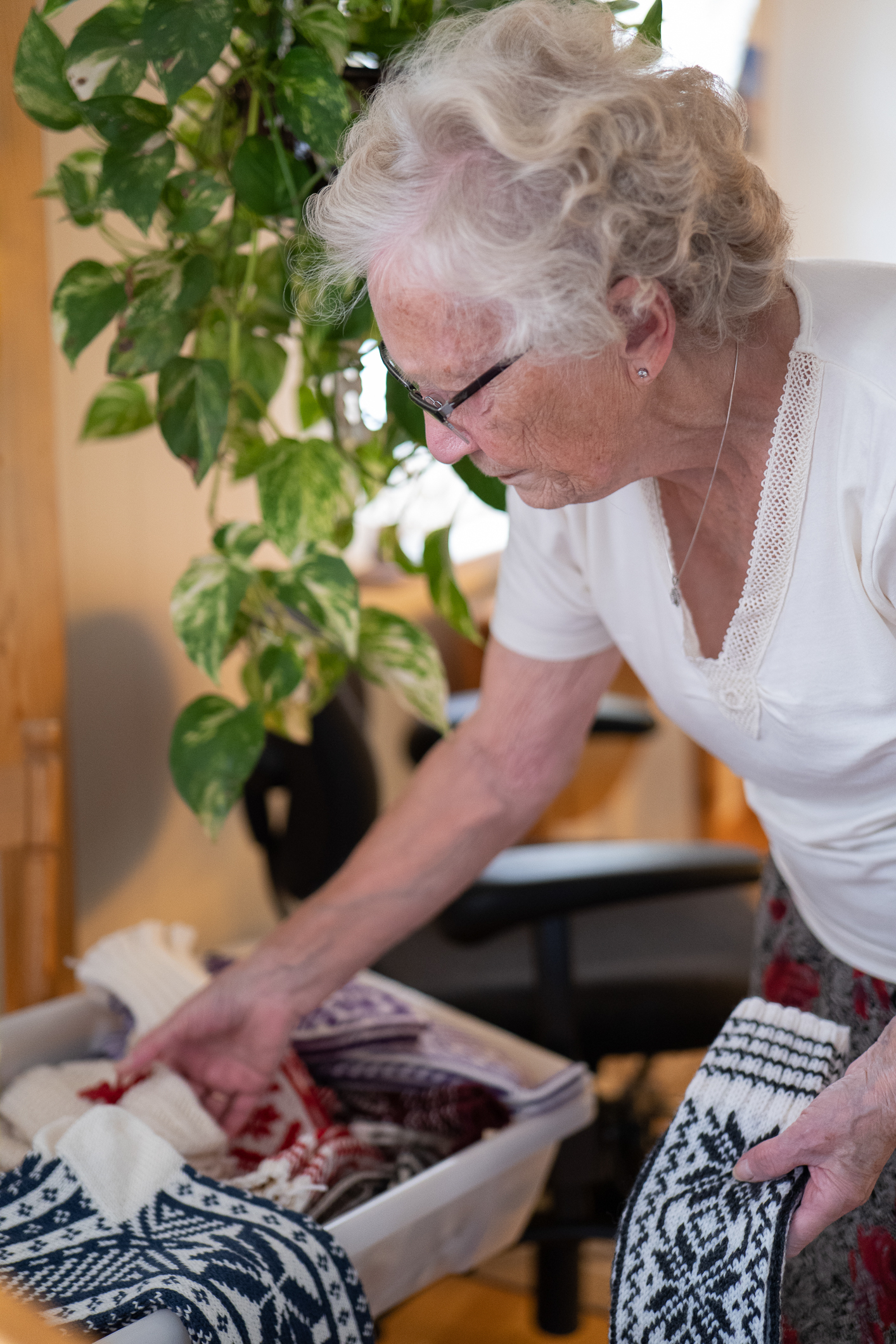 Kvinne med hvitt hår  og briller viser fram strikkede selbuvotter og sokker i blått og hvitt