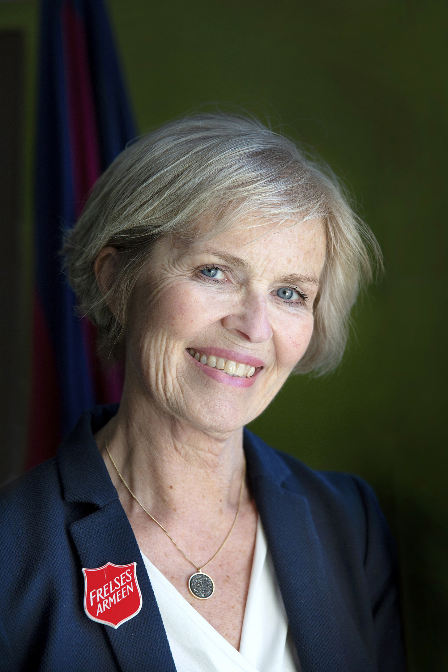 Et portrettbilde av avdelingsleder Solfrid Slettholm. Mørk bakgrunn. Hun har Frelsesarmeens skjold festet til jakkeslaget. Hun smiler.