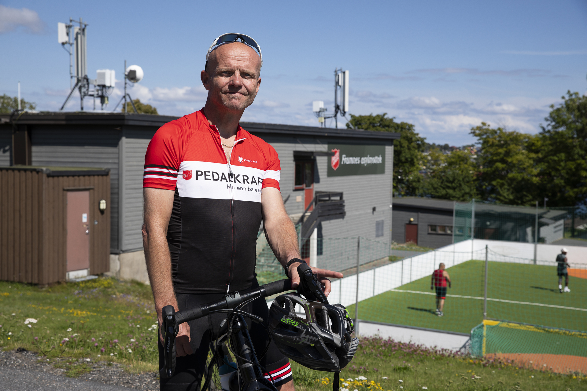 Foto: Mann står oppstilt med sykkelen i fullt utstyr. I bakgrunnen sees en fotballbinge.