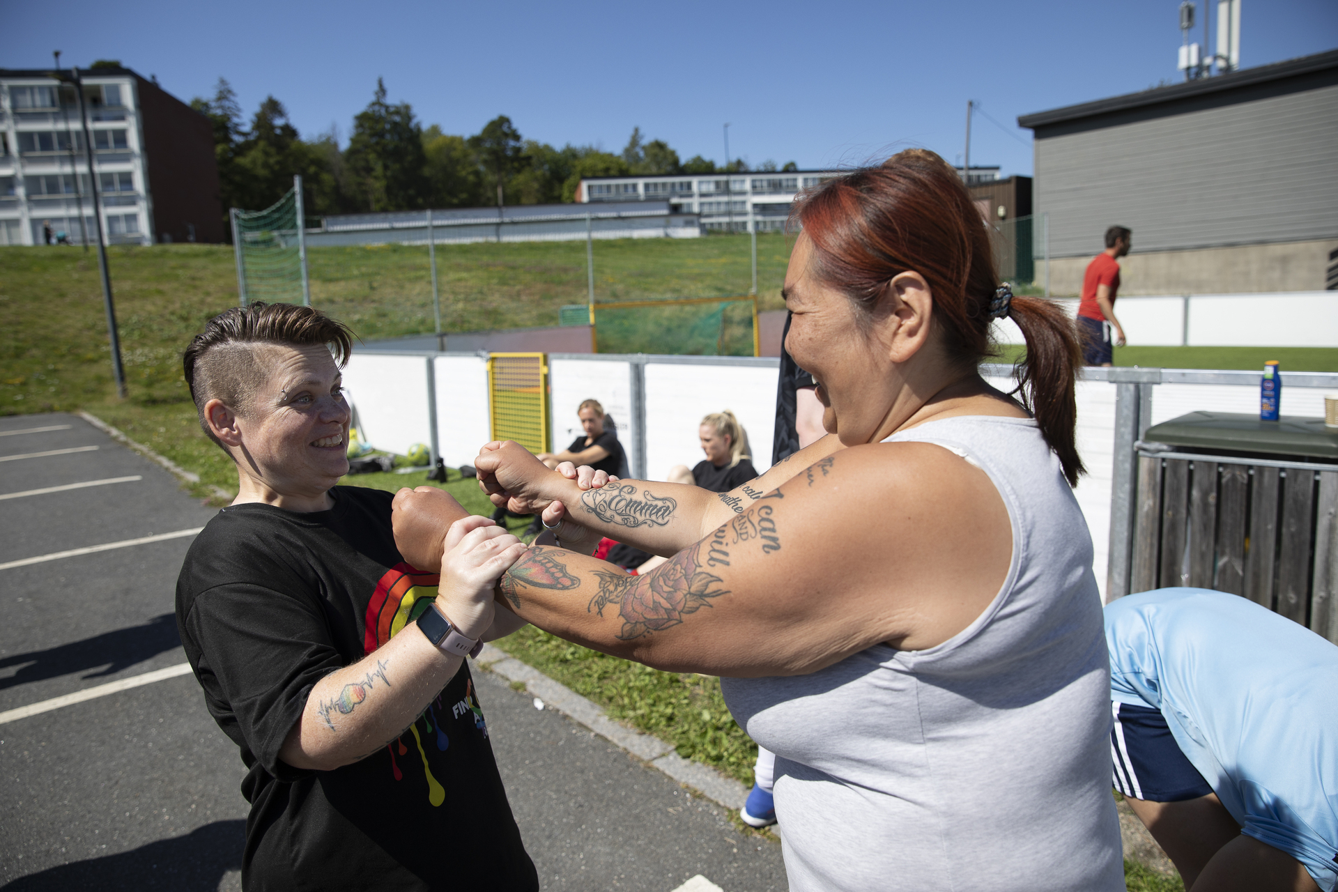 Foto: To kvinner med tatoveringer holder hverandre i armene og ler like utenfor fotballbingen.