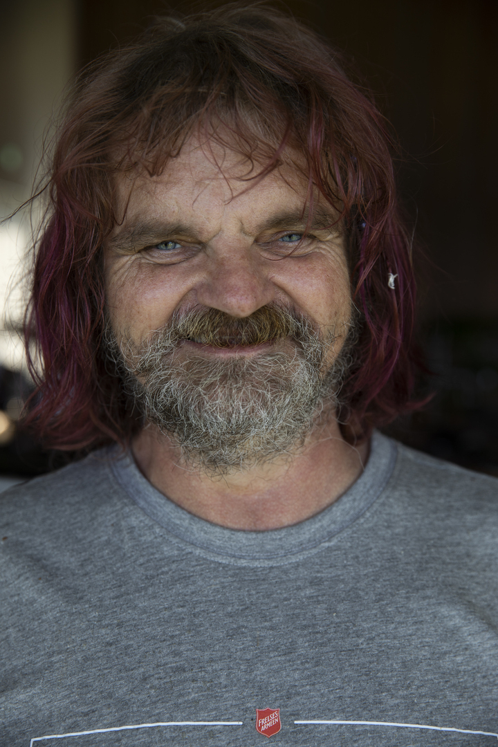 Foto: Mann med lengre hår og grått skjegg i grå T-skjorte med logo fra Frelsesarmeen. Ser i kamera.