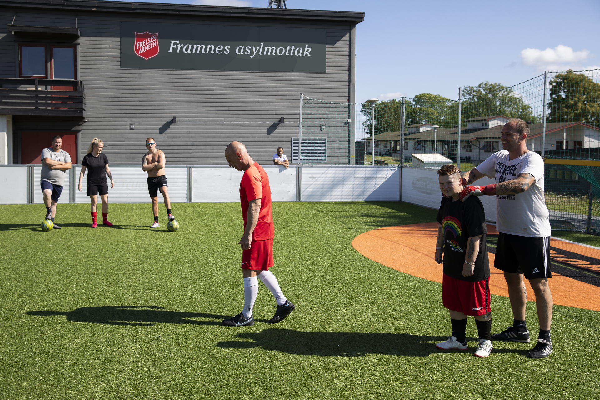 To foto etter hverandre: Det første viser en ballbinge med seks spillere. En spiller knar en annen på skuldrene. De venter på å sette i gang spillet. På et skilt på en vegg rett bak dem, står det Framnes asylmottak ved siden av Frelsesarmeens logo. Det andre bildet er av en legg med en stor tatovering på og en annen fot med sandal..