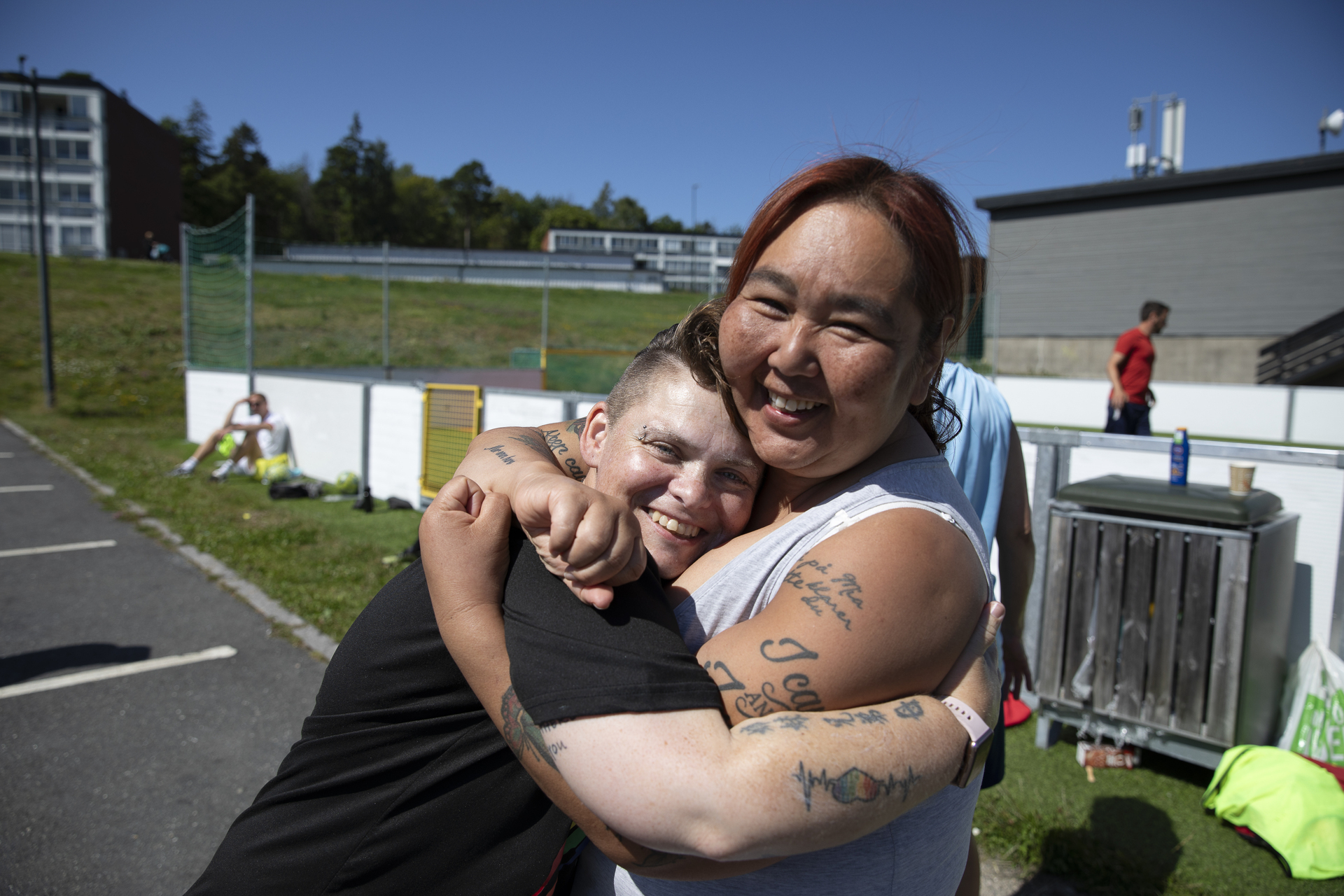 Foto: To kvinner klemmer hverandre hardt utenfor en ballbinge. Begge har tatoveringer og sparker fotball.