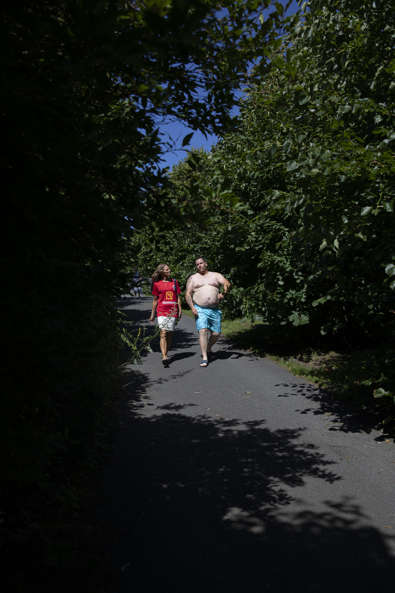 Foto: Mann og kvinne går på en smal vei. Grønne trær på begge sider.