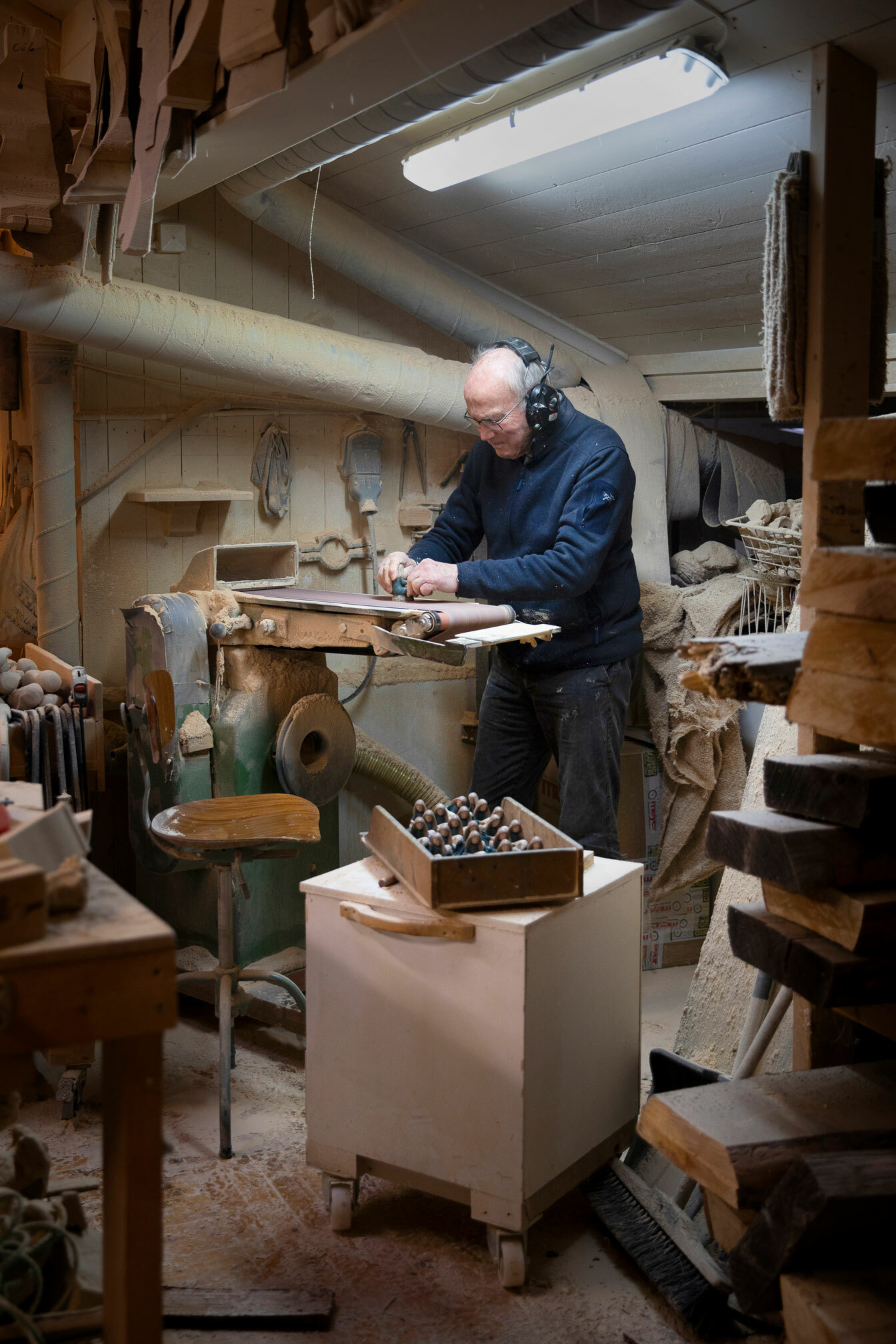Foto: Skallet, eldre mann med briller står ved en pussemaskin i form av et belte som ruller. Han pusser på en figur.