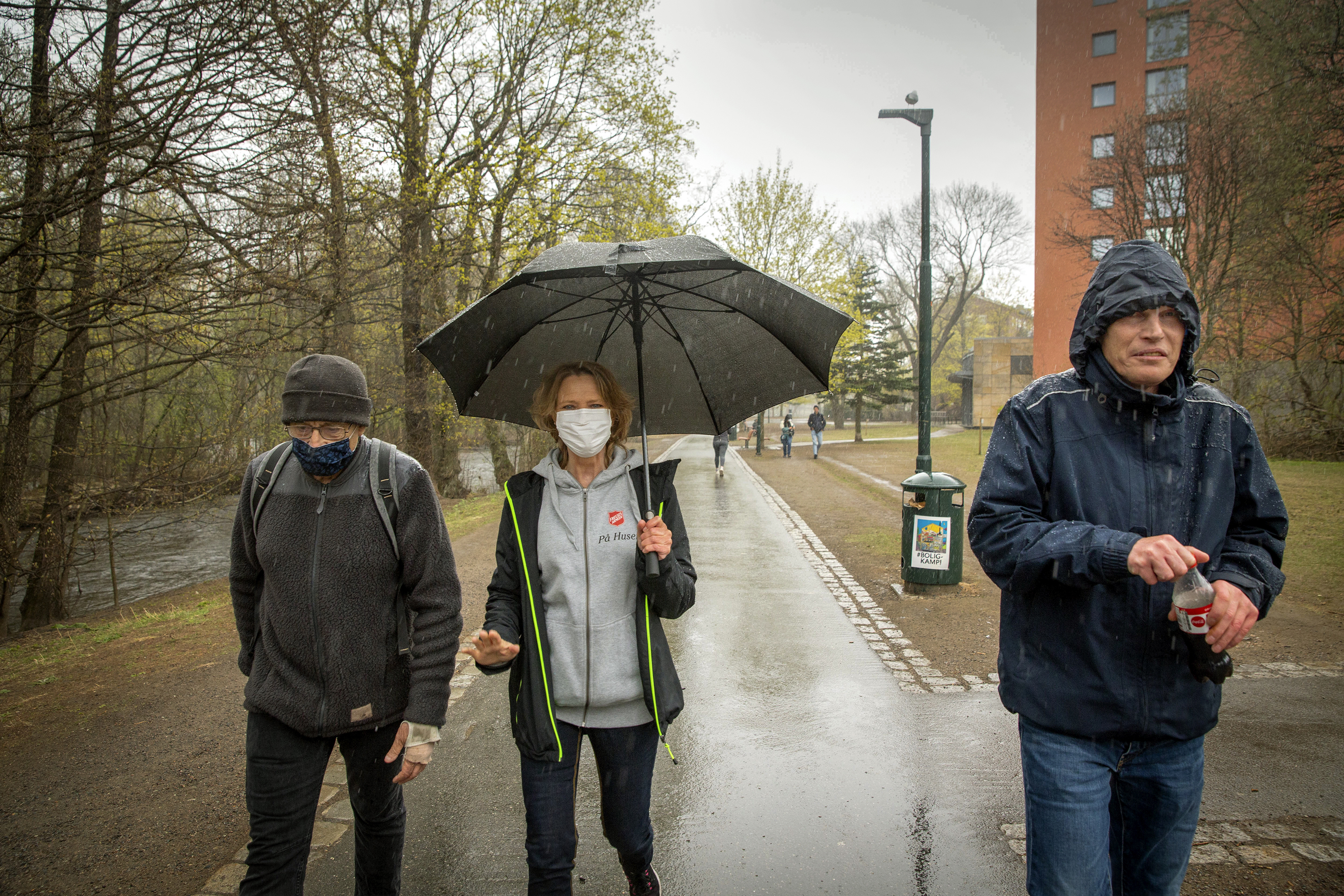 Tre turgåere med munnbind, paraply og regnfrakk