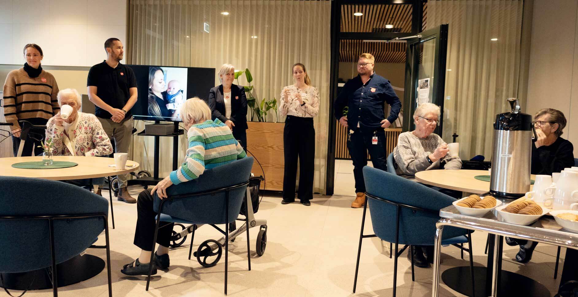 En gruppe ledre kvinner sitter rundt noen bord og tre kvinner og to menn står foran og snakker til forsamlingen