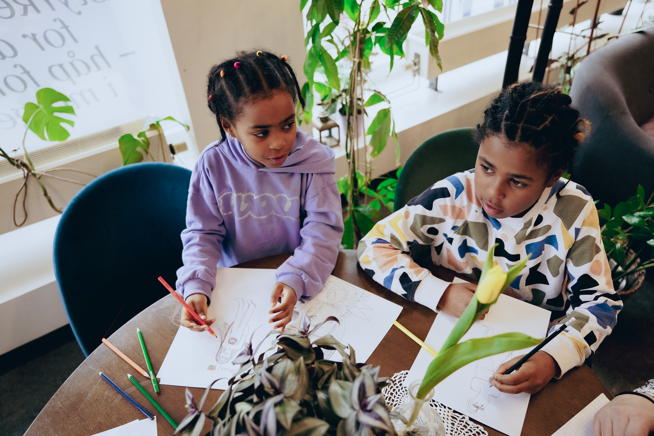 To jenter sitter og tegner ved et rundt bord