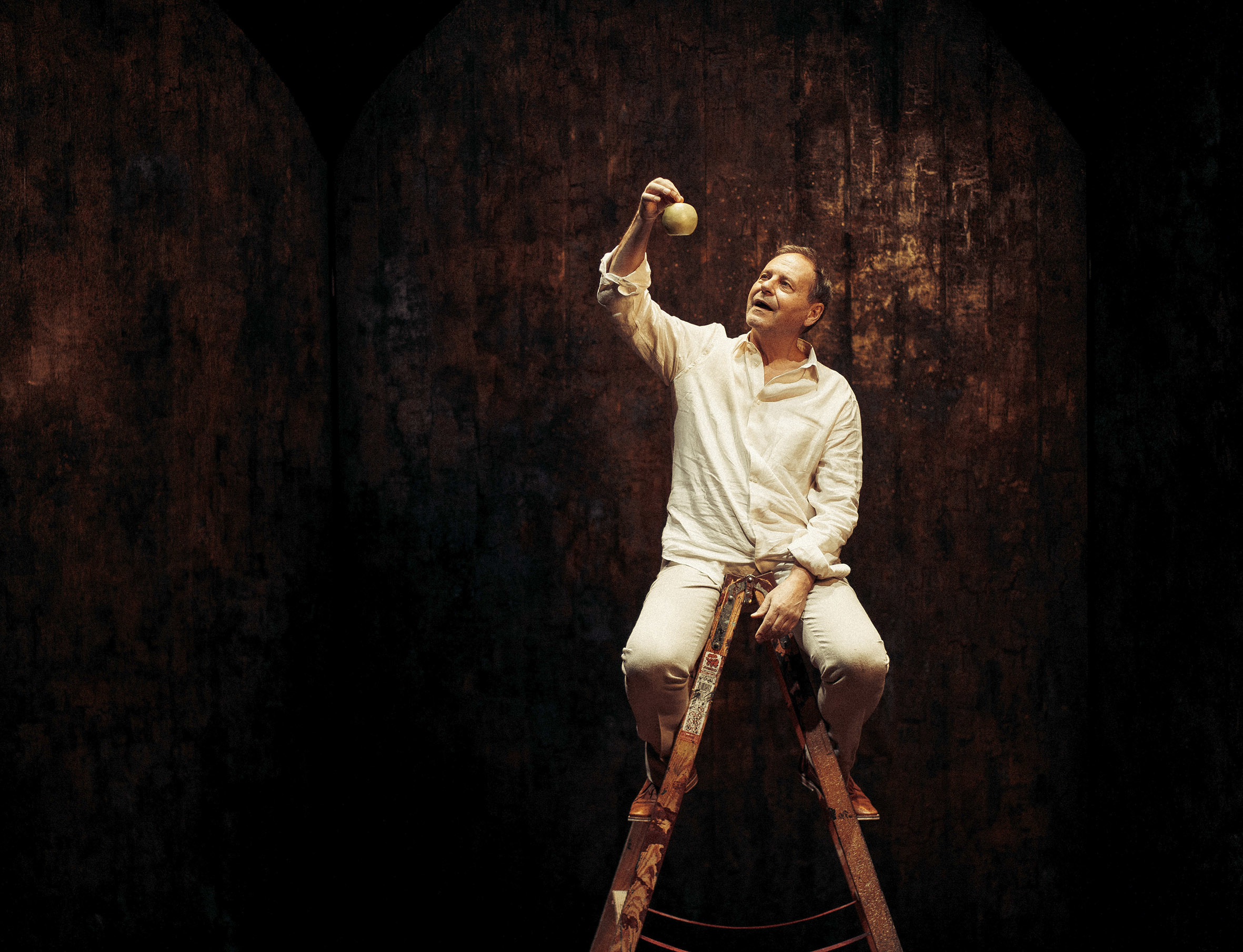 Svein Tindberg sitter på en gardintrapp med et eple i hånden, under stykket Gudspartikkelen.