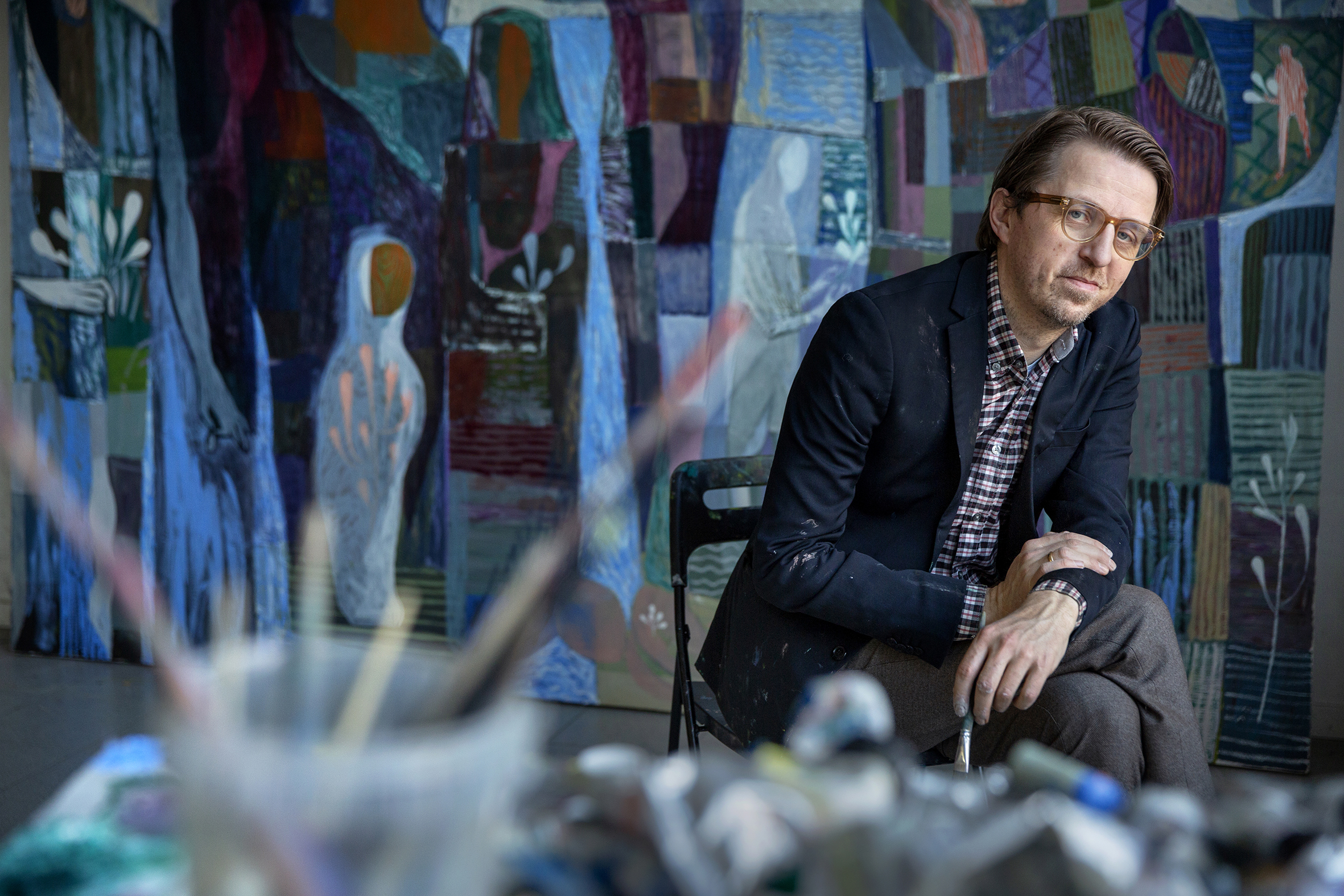 Sverre Bjertnæs sitter foran et stort maleri i sitt atelier.