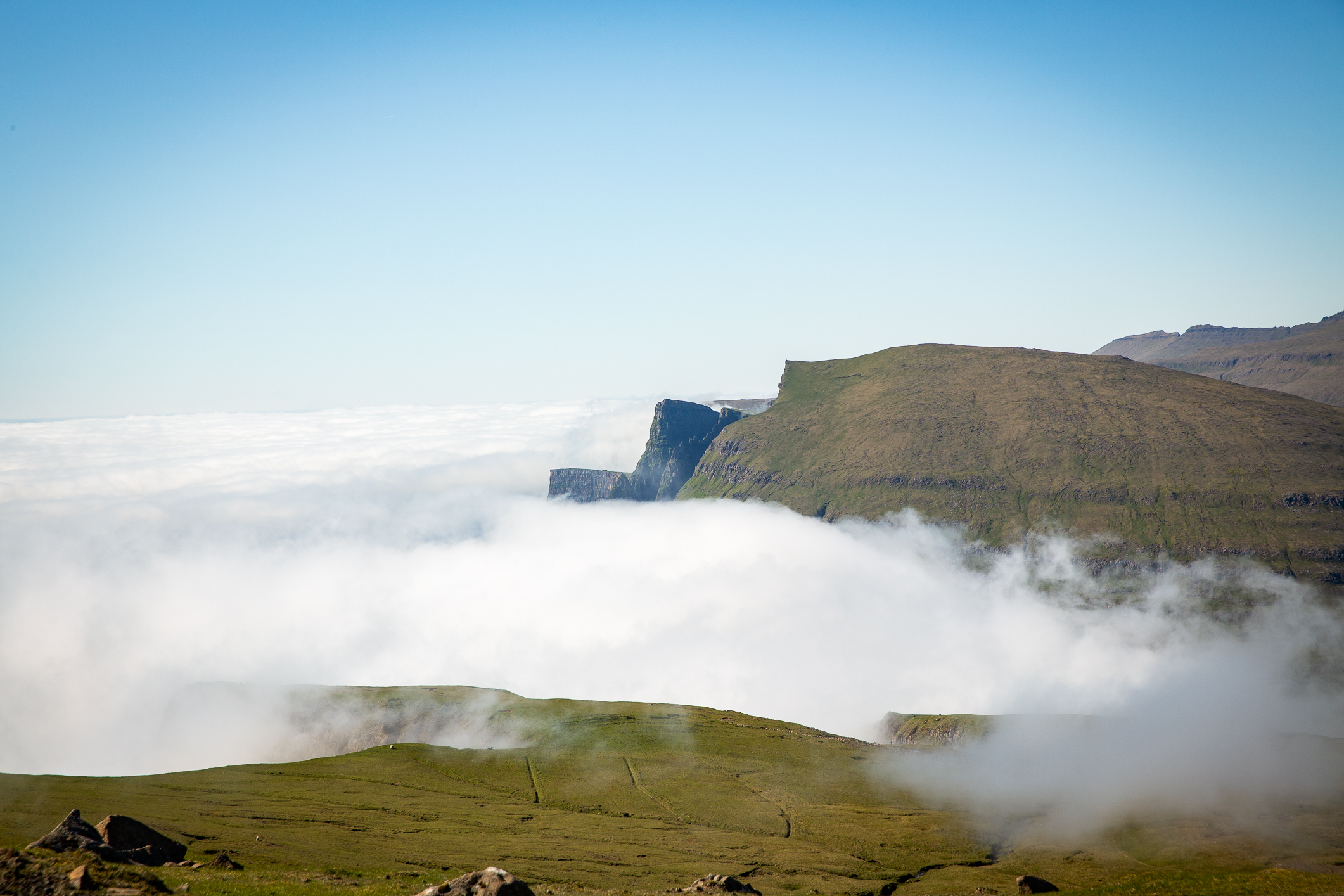 Skodde ligger over bare, grønne klipper høyt over havet.