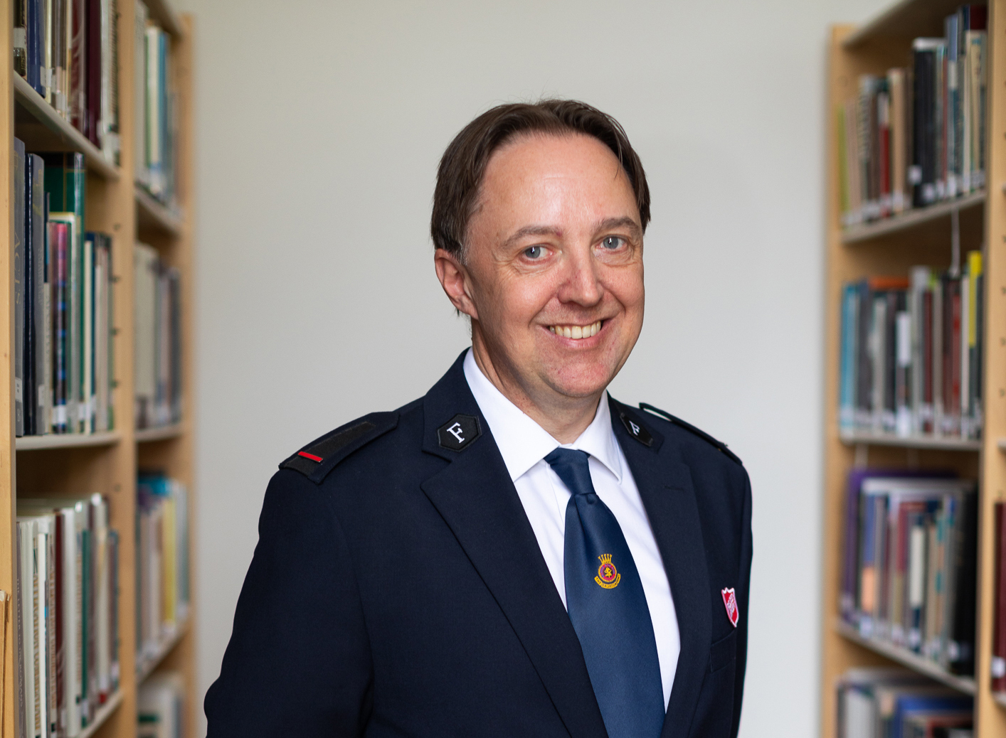 Mann står i et bibliotek med hyller av bøker på begge sider. Han har på seg uniform fra Frelsesarmeen.