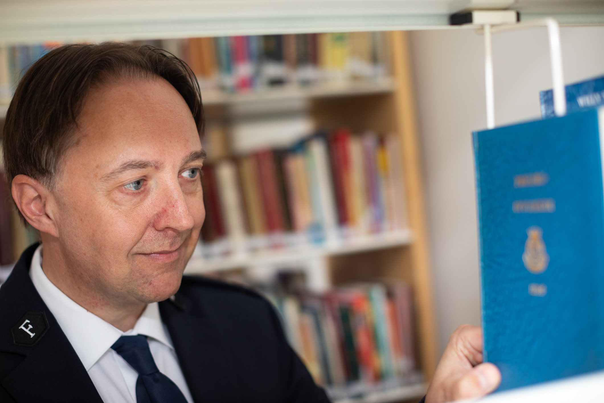 Nærbilde av mann i uniform som drar en bok ut av en bokhylle.