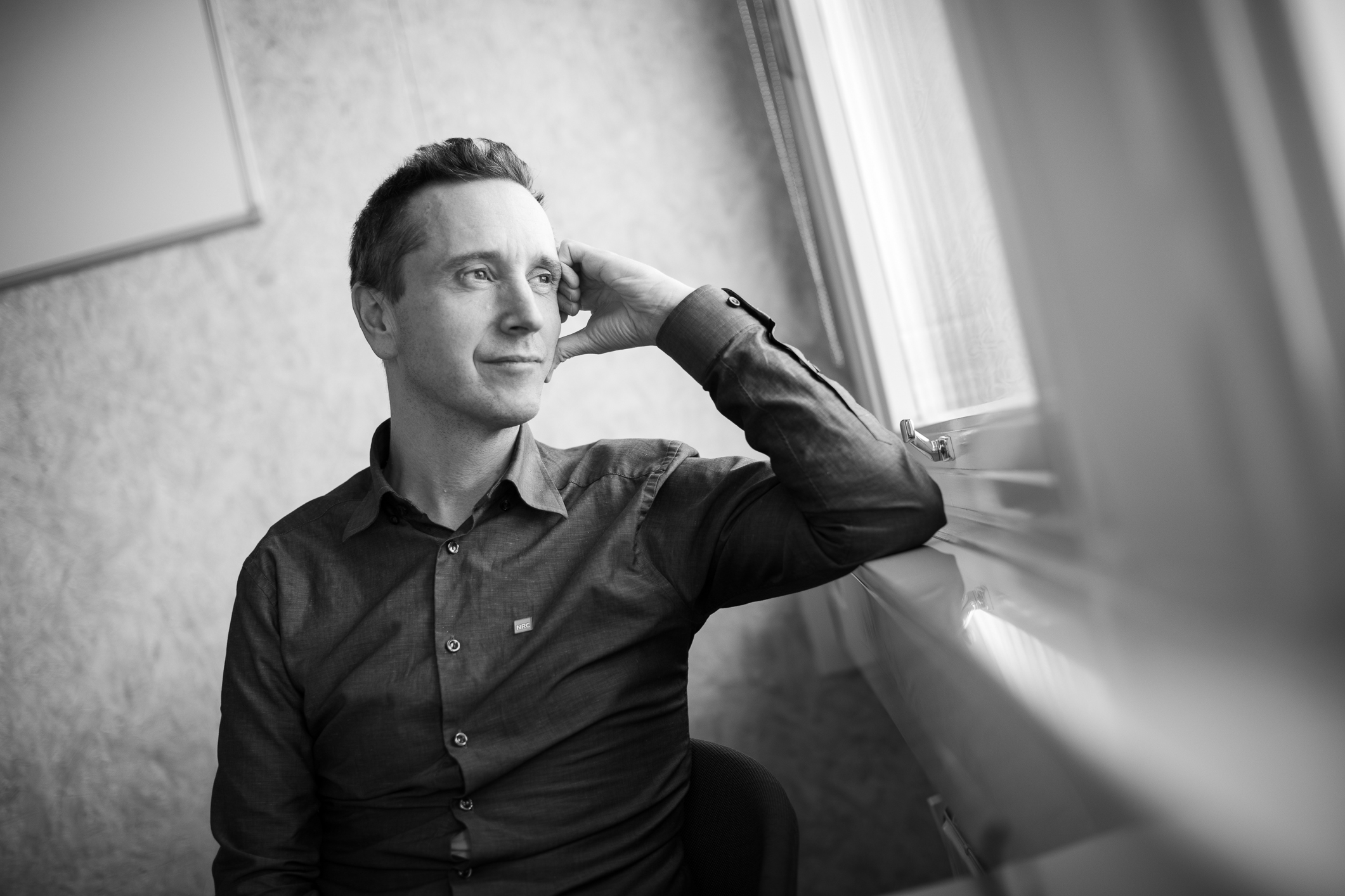 Sort-Hvitt bilde av mann som står og ser ut av vindu. Albuen er plantet i vinduskarmen som er høyt oppe på veggen.