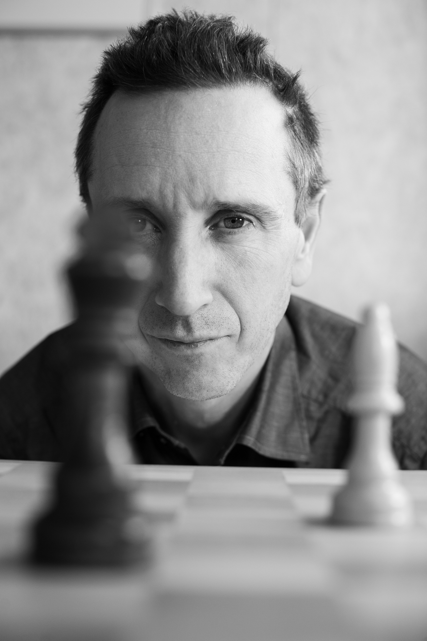 Bilde i sort-hvitt med et hode som stikker opp bak et sjakkbrett med svart konge og hvit løper.