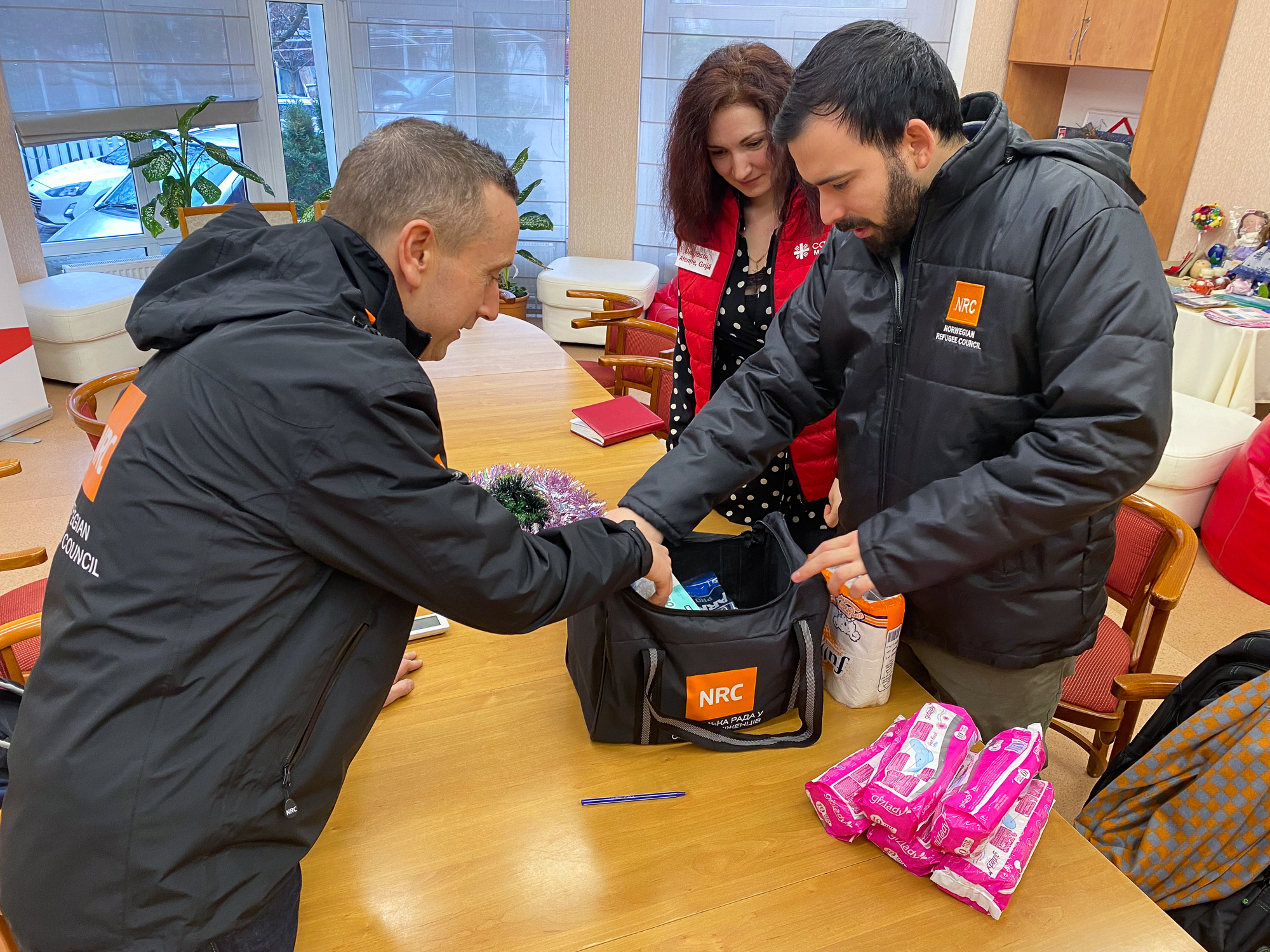 To menn i jakker fra Flyktninghjelpen sjekker en liten bag med innhold. En kvinne står litt lenger bak og ser på. Bildet er tatt inne på et kontor i Moldova.