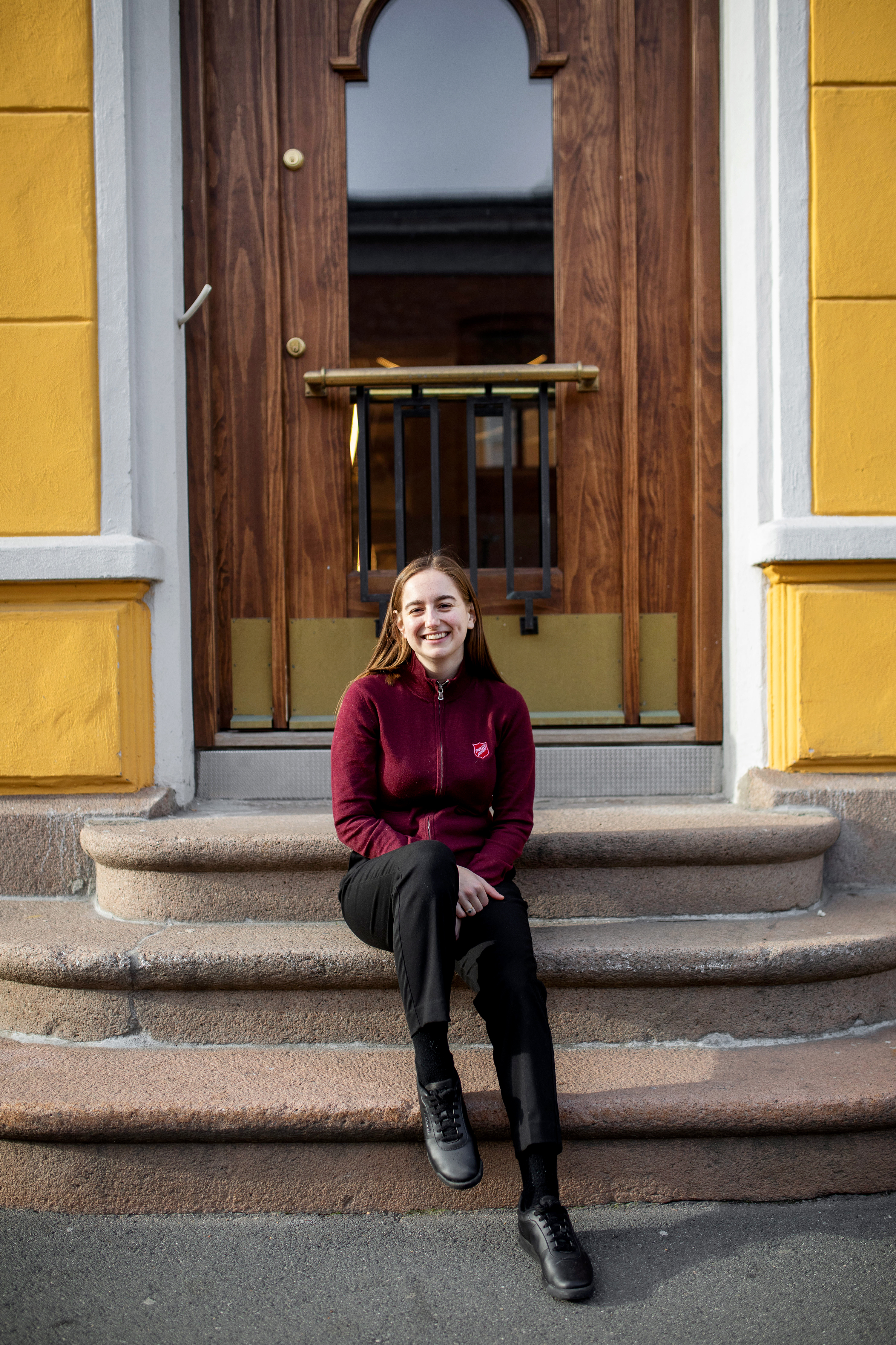 Trude Pettersen sitter på en murtrapp foran en stor eikedør til et gult murhus