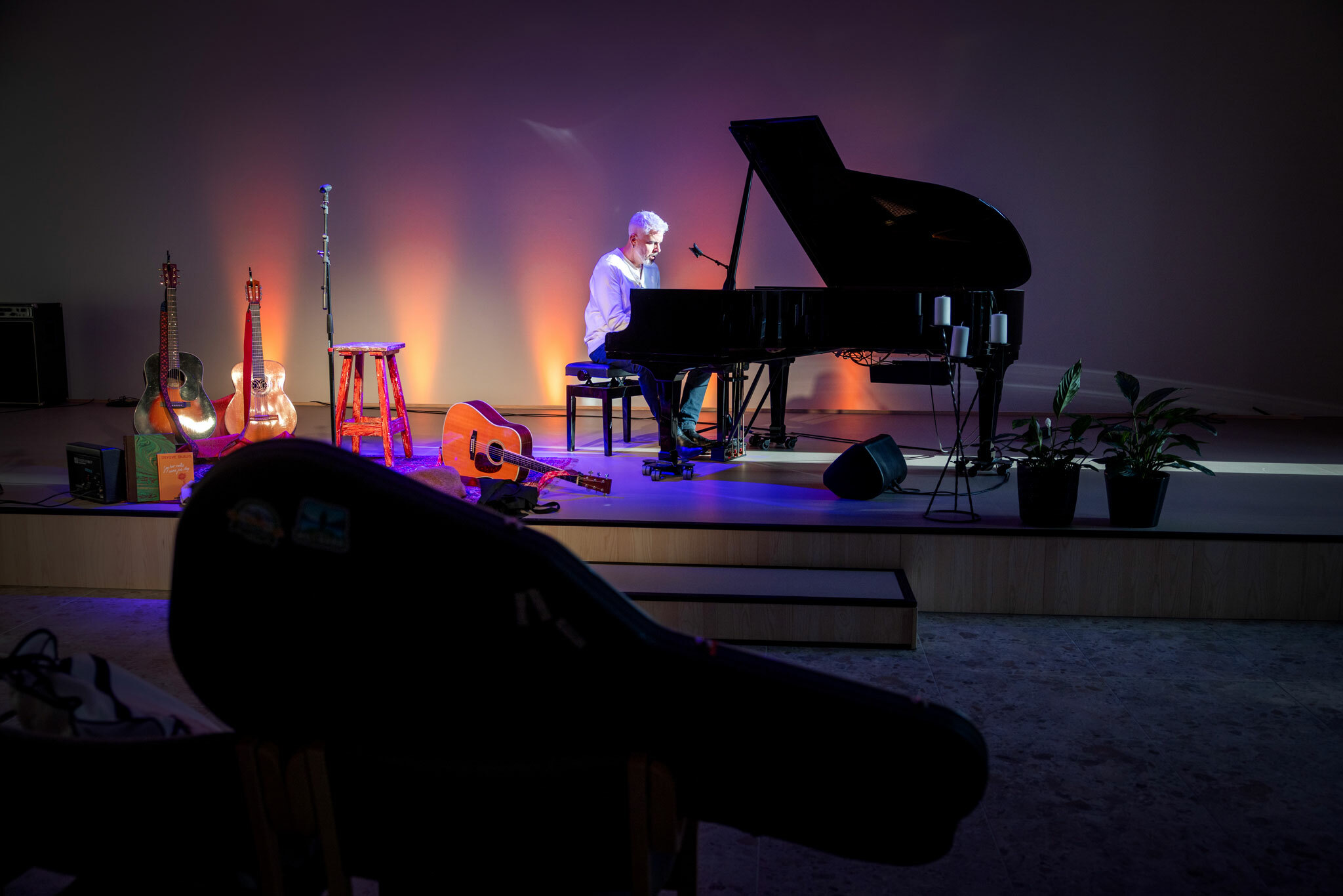 Foto: Mann med bleket hår og grått skjegg sitter og spiller ved et flygel. Rundt ham er det flere instrumenter på scenen.