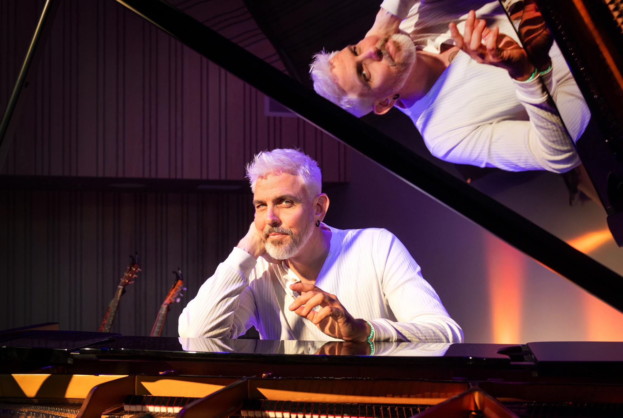 Foto: Mann sitter bak et flygel. Gjennom åpningen ses hans refleksjon i det svarte, blanke lokket.