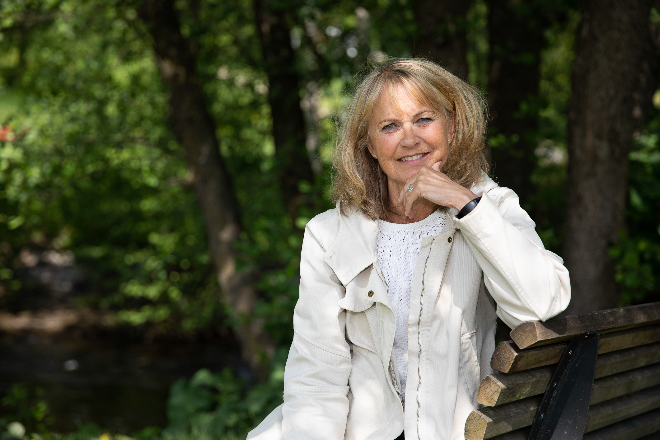 Smilende kvinne sitter ute på en benk. Natur bak.