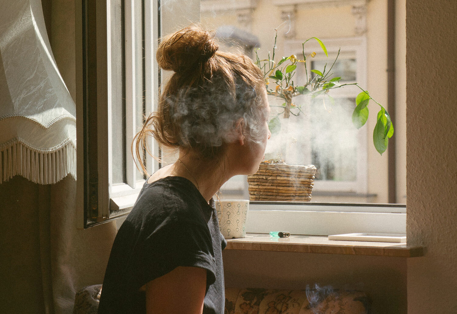 Kvinne stirrer ut av vinduet i et røykfylt rom.