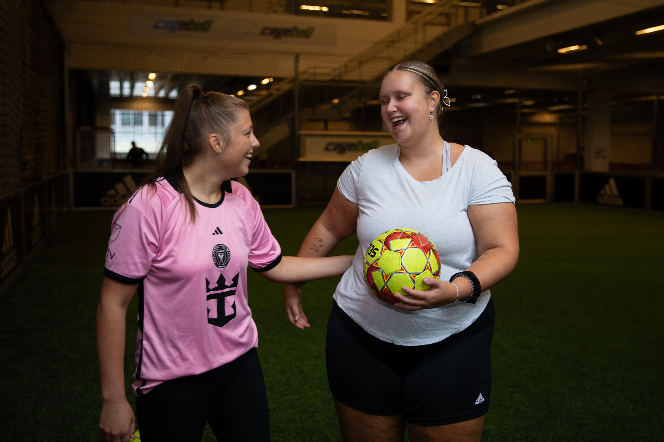 To unge gatefotballspillere står og smiler mot hverandre. Den ene holder en fotball.