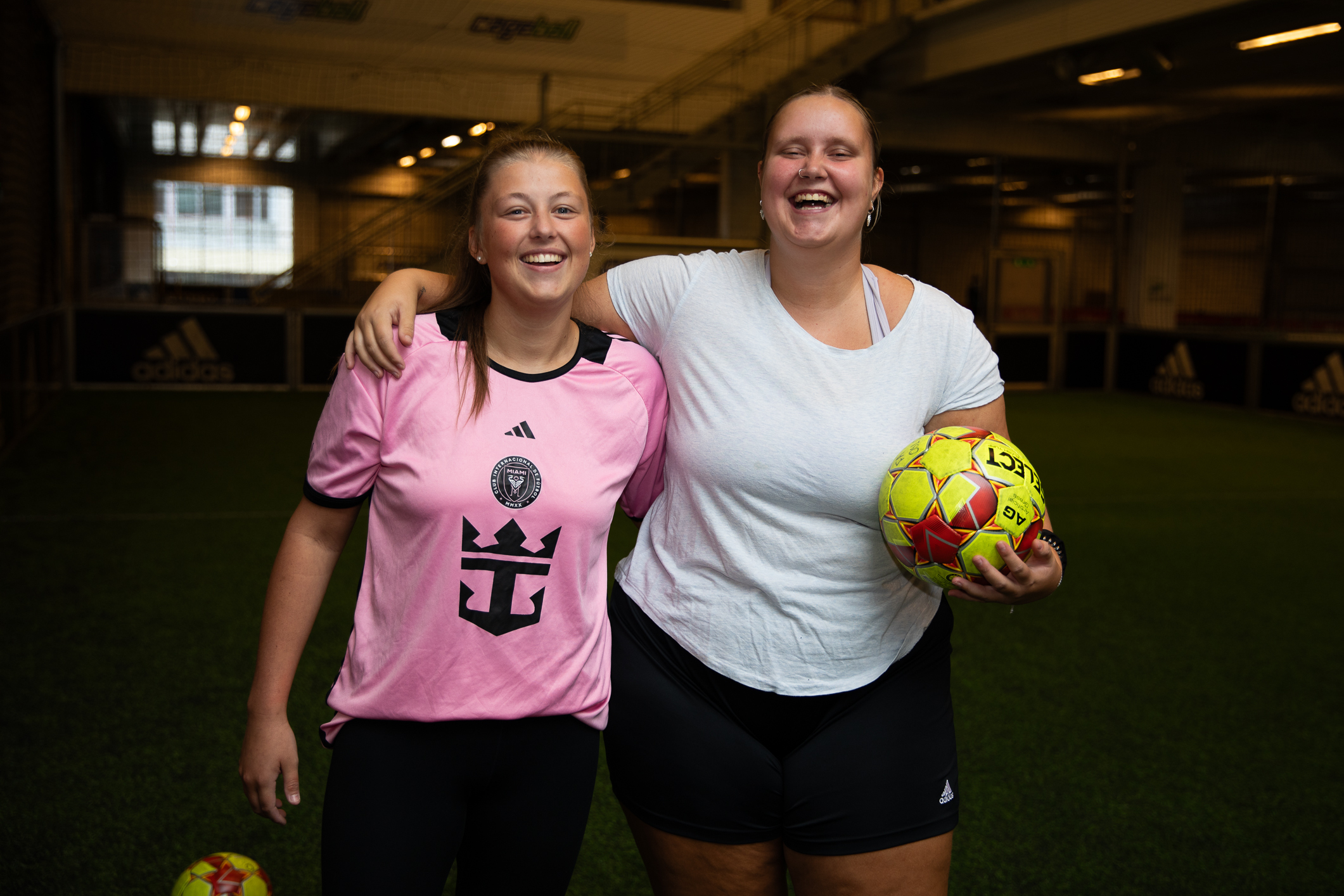Foto: To smilende fotballspillere i 20-årene holder rundt hverandre. Ser inn i kamera, den ene holder en fotball.