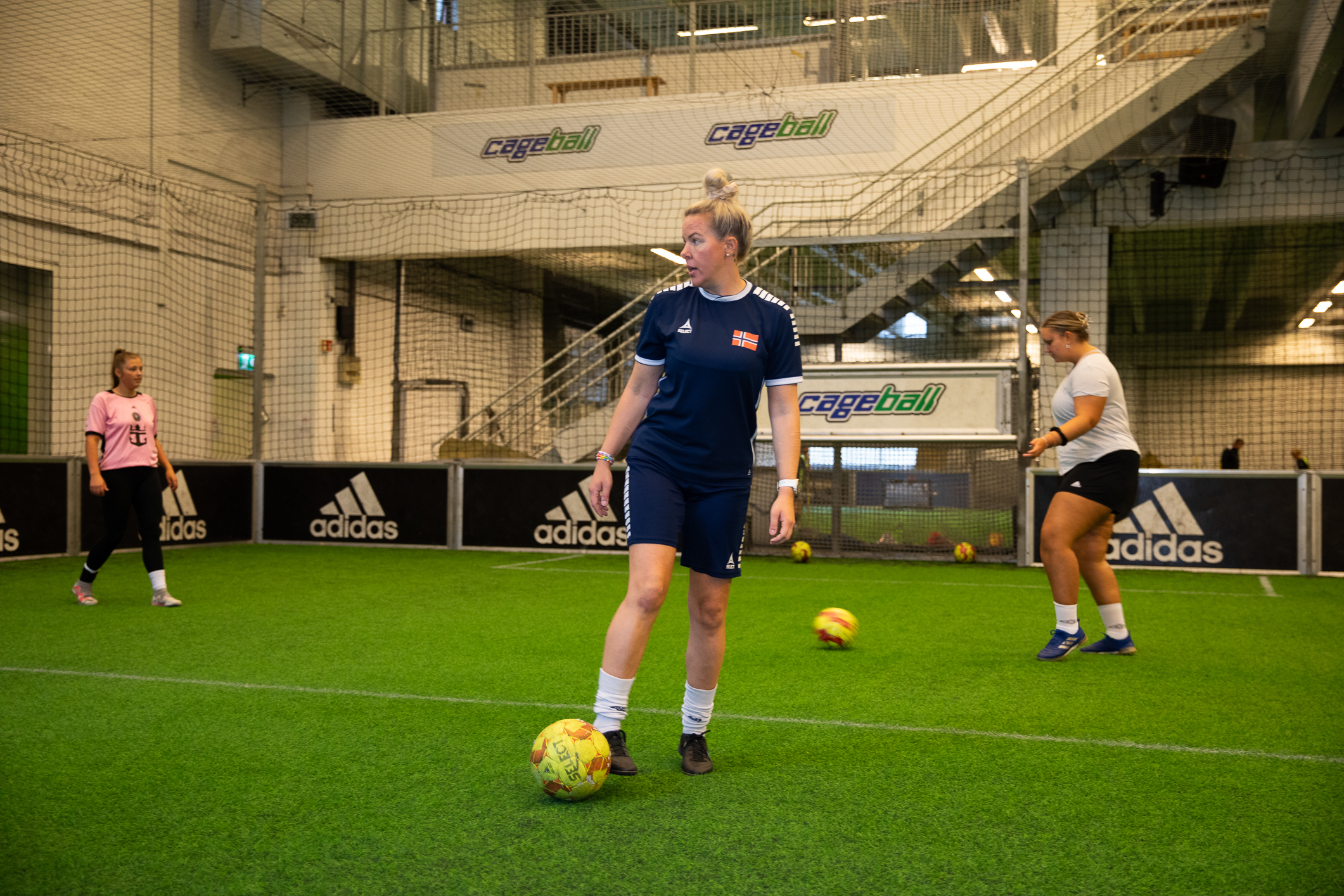 Foto: Tre kvinner spiller fotball på en innendørsbane.