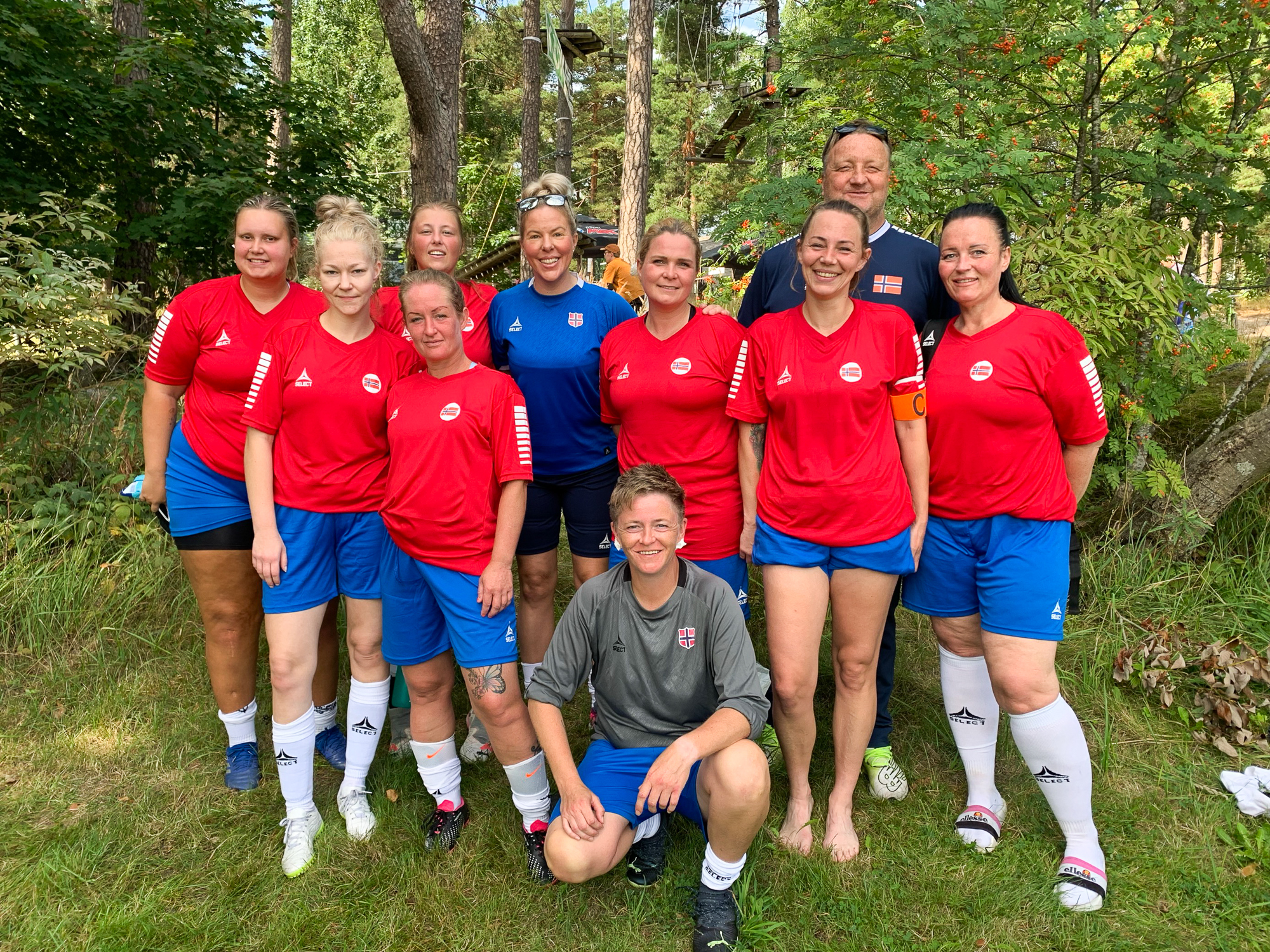 Foto: Lagbilde av kvinner i røde og blå fotballdrakter, tatt ute i naturen.