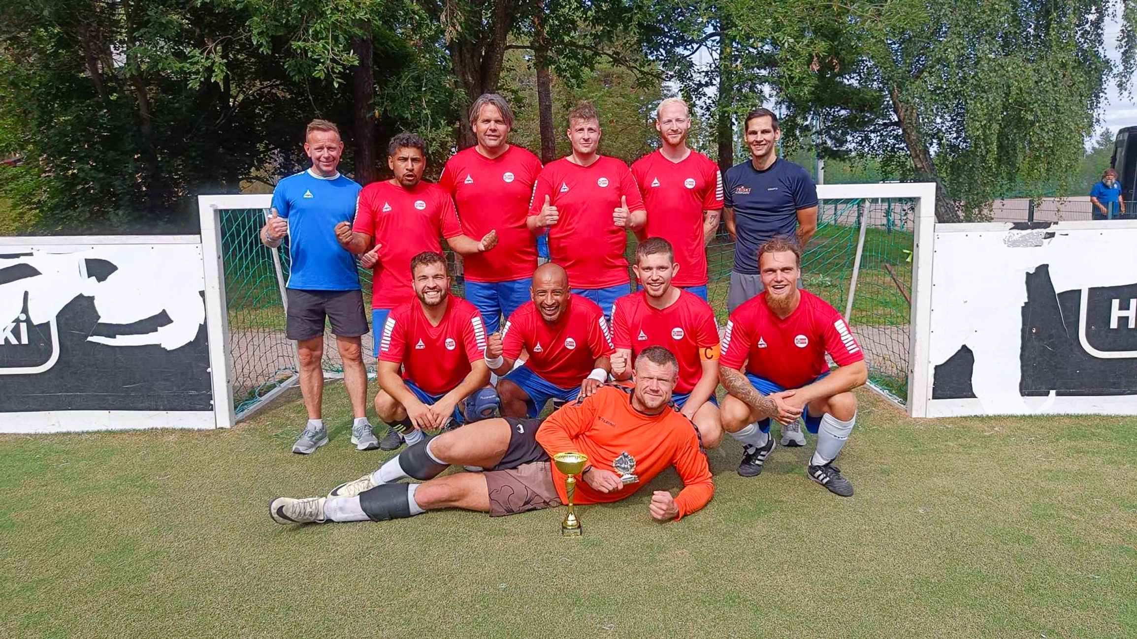 Foto: mannlige spillere i røde og blå drakter er stilt opp foran et gatefotballmål og ser inn i kamera