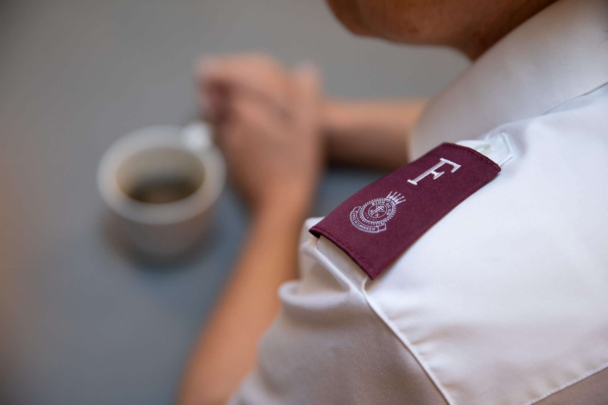 Skulderpartiet til en med Frelsesarme-uniform. Kaffekopp på bordet.