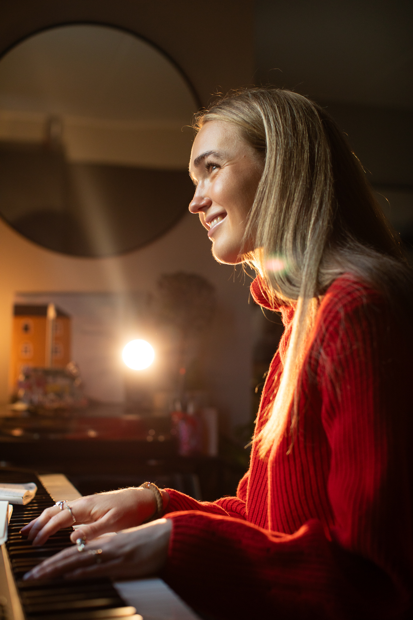 Kvinne med langt hår sitter og spiller piano. Vi ser henne fra siden der hun sitter og smiler litt.