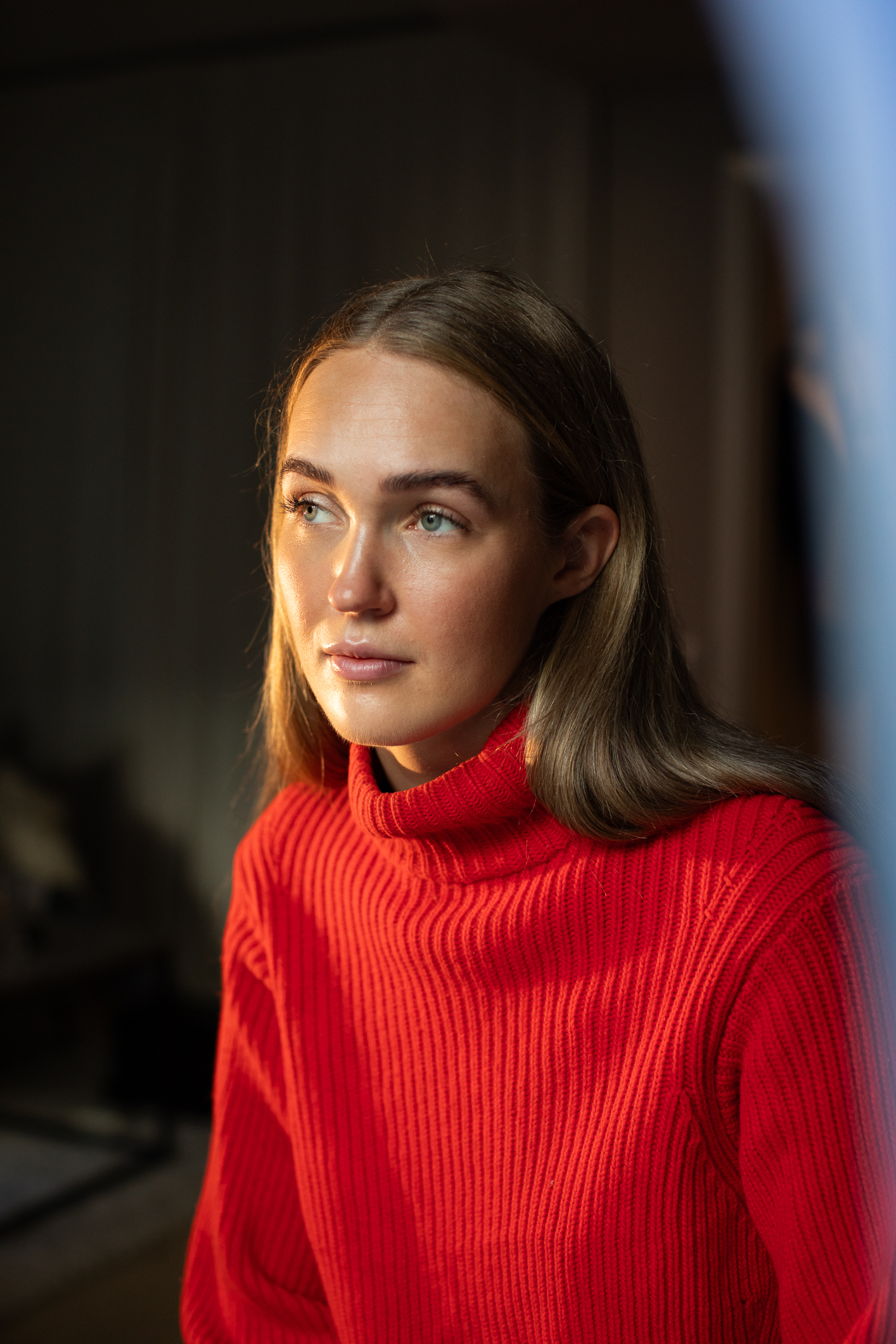 Kvinne med langt hår og rød genser har festet øynene på et punkt bortenfor fotografen.