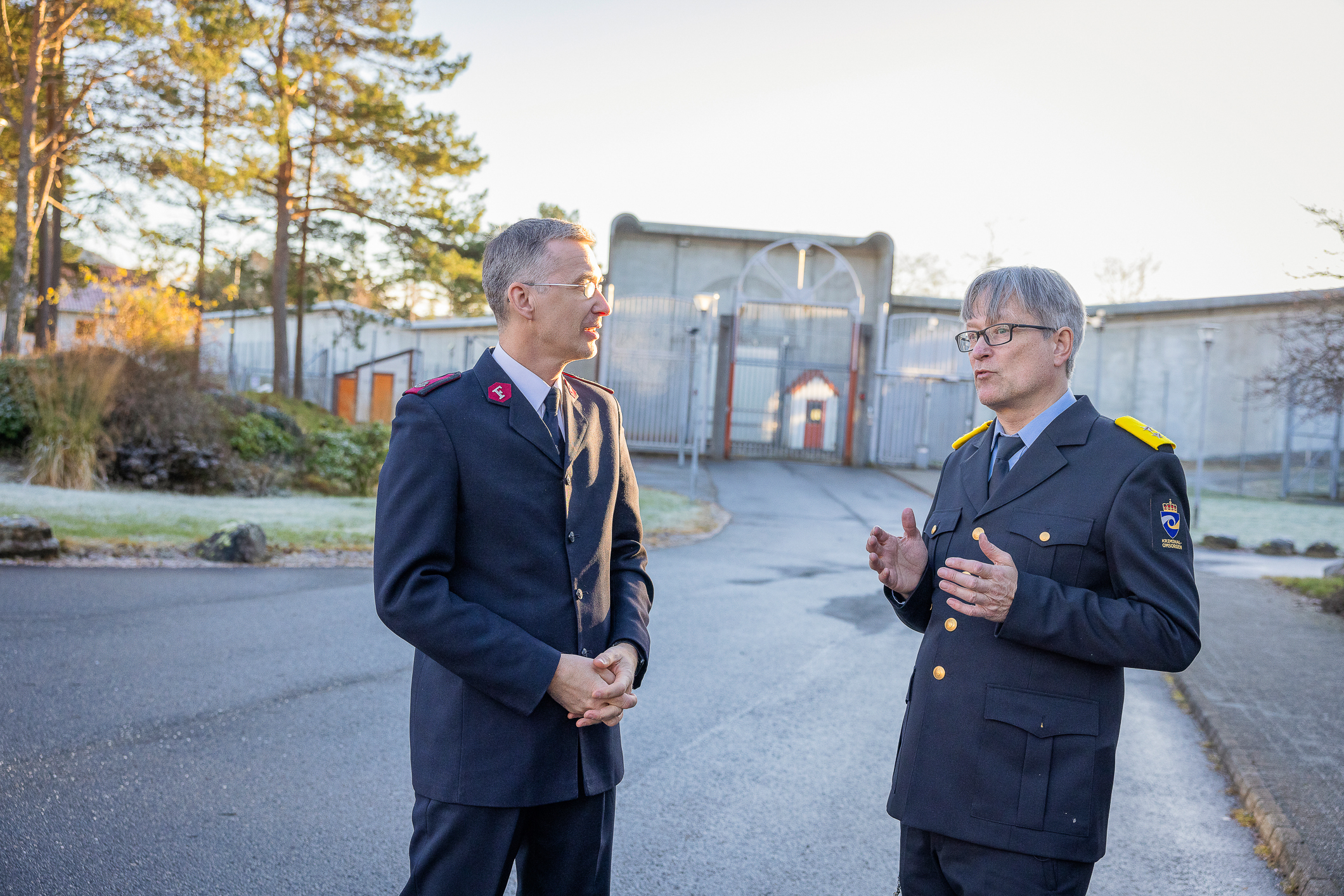 To menn, den ene med frelsesarméuniform, den andre med kriminalomsorgens uniform med fengselsmurer bak
