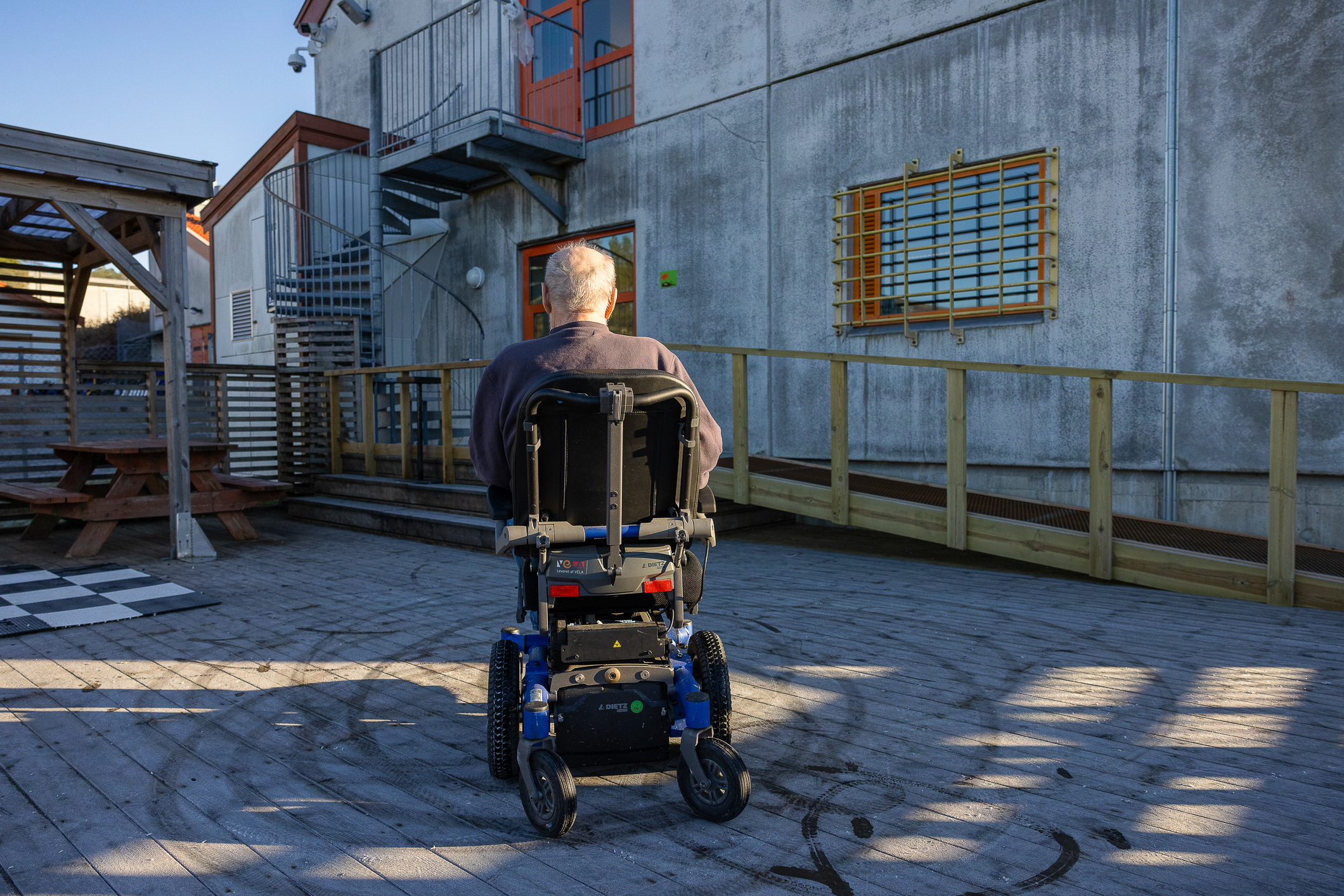 Mann i elektrisk rullestol i en luftegård med fengselsmurer bak.