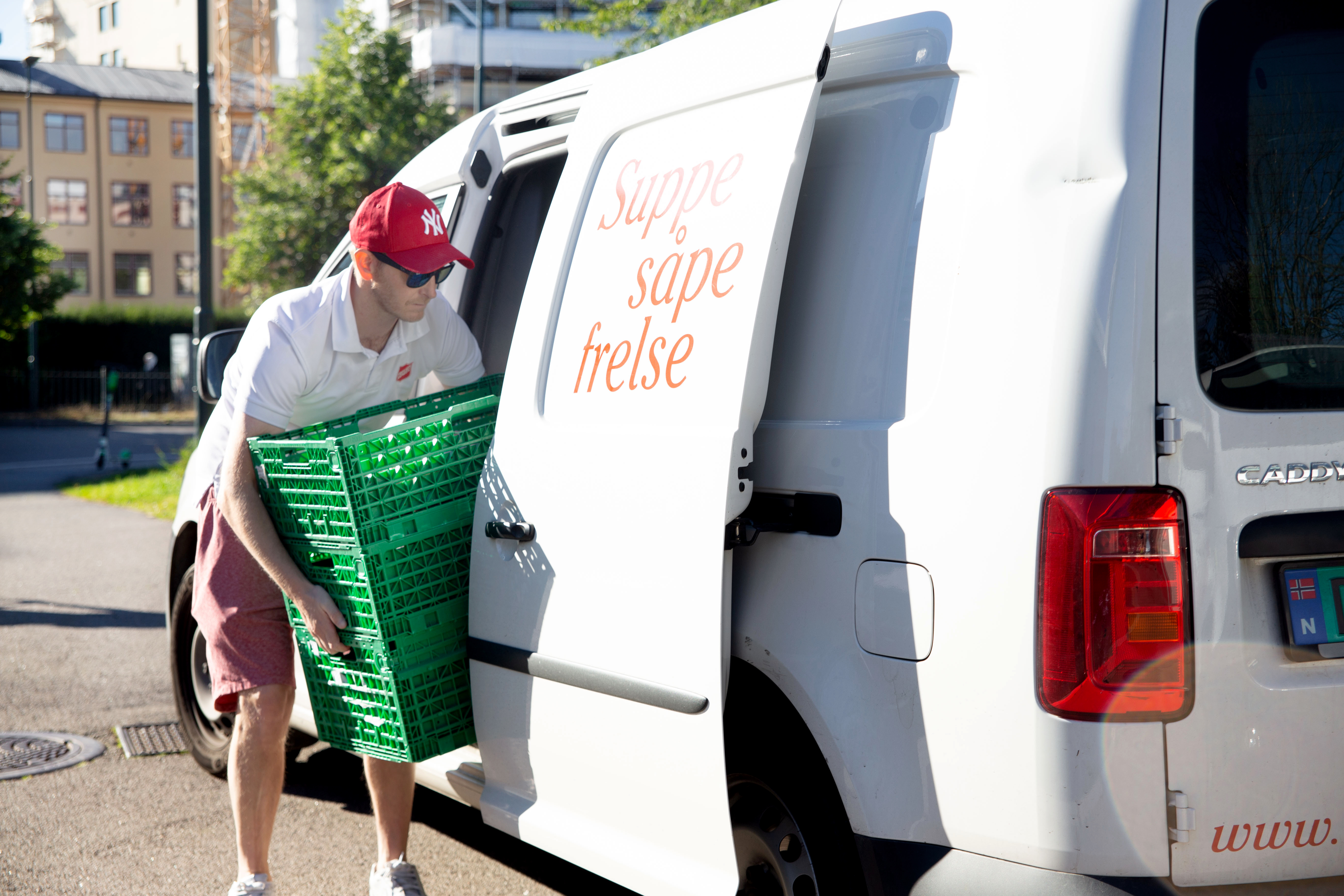Mannlig sjåfør i Frelsesarme-uniform laster inn en kasse i varebil. Bilde tatt fra siden.