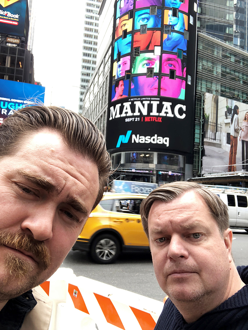 Espen (t.h) står sammen med kamerat og medforfatter Håkon Bast Mossige på Times Square i New York. Bak dem fylles en vegg med reklmae for nyinnspillingen av "Maniac"