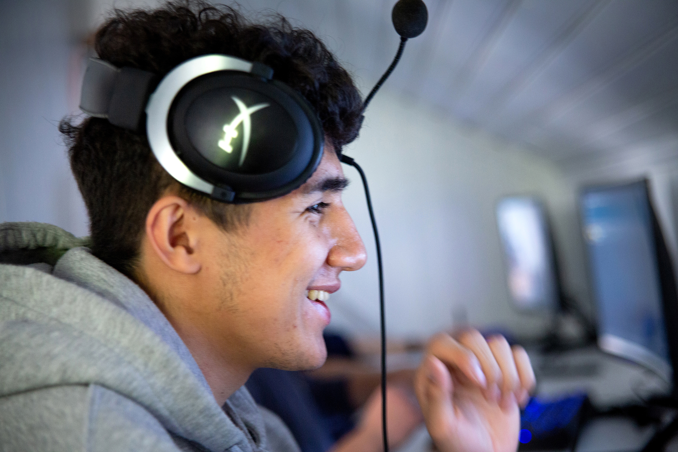 Det første bildet viser en ung mann som sitter og smiler mot en dataskjerm, han har flyttet headsettet bort fra ørene. Det andre bildet viser en annen ung mann som sitter med headsett og snakker med en annen person som kan skimtes i forgrunnen.