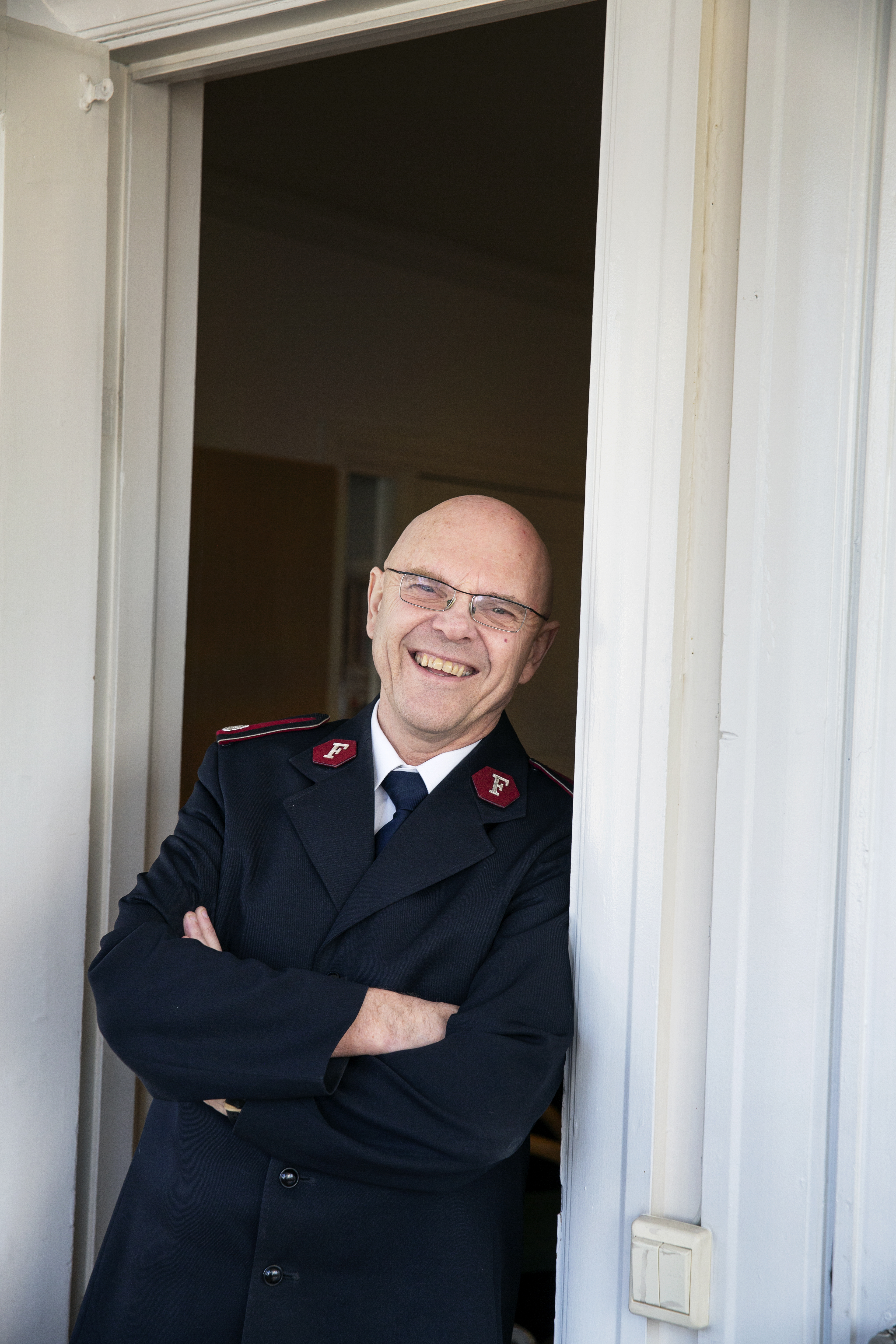 Til venstre ser vi Bernt Olaf Ørnes. Han har på seg Frelsesarmeens offisersuniform. Hen lener seg mot en dørkarm med armene i kors og smiler. Mona Rindal Rasmussen står foran et halvåpent vindu halvveis dekket av bondegardiner.Hun ser skrått forbi fotografen mot noe lenger borte.