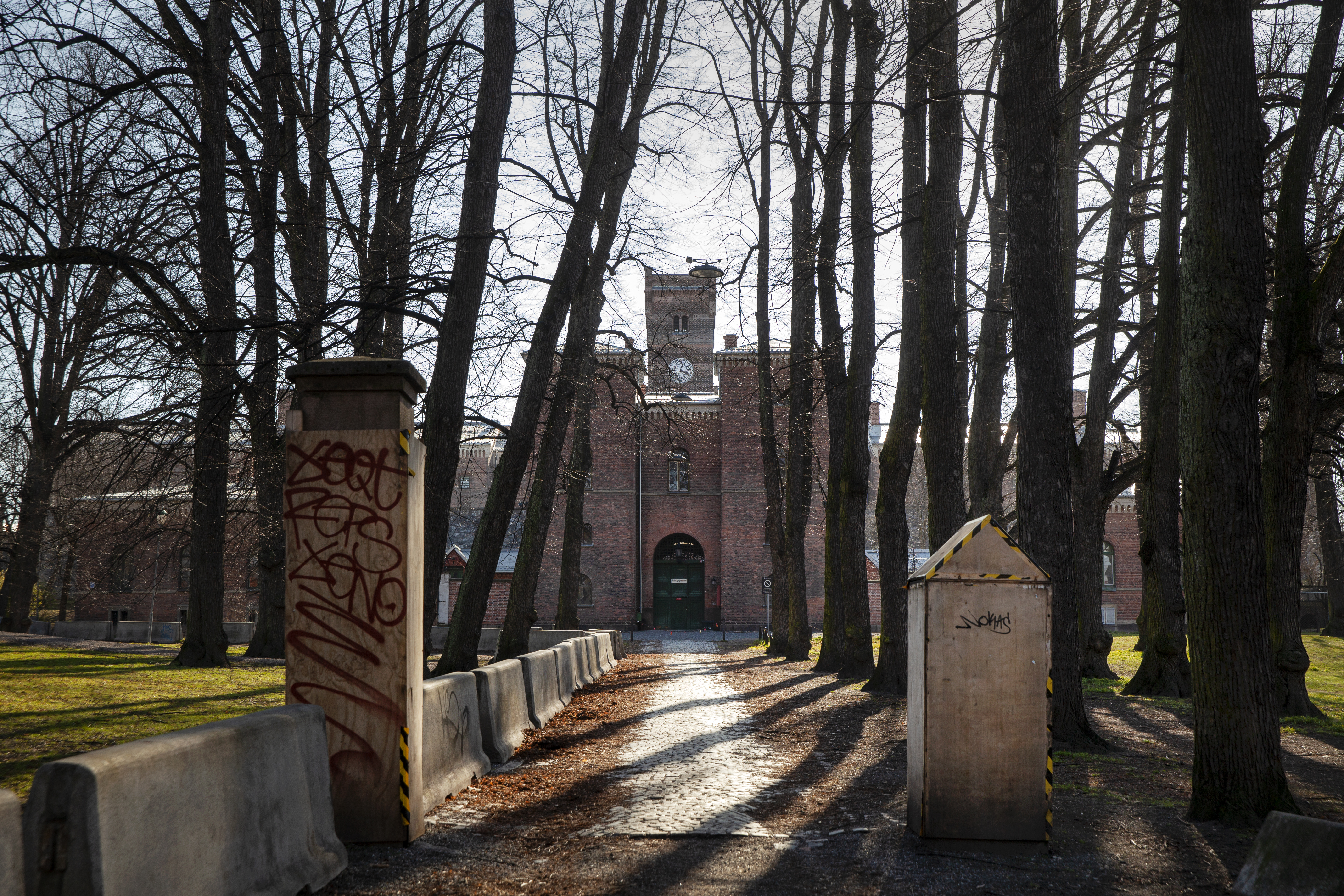 Bildet er tatt ved porten til veien som leder til inngangsdøren til Oslo fengsel. Sollyset titter frem mellom de bladløse trærne.