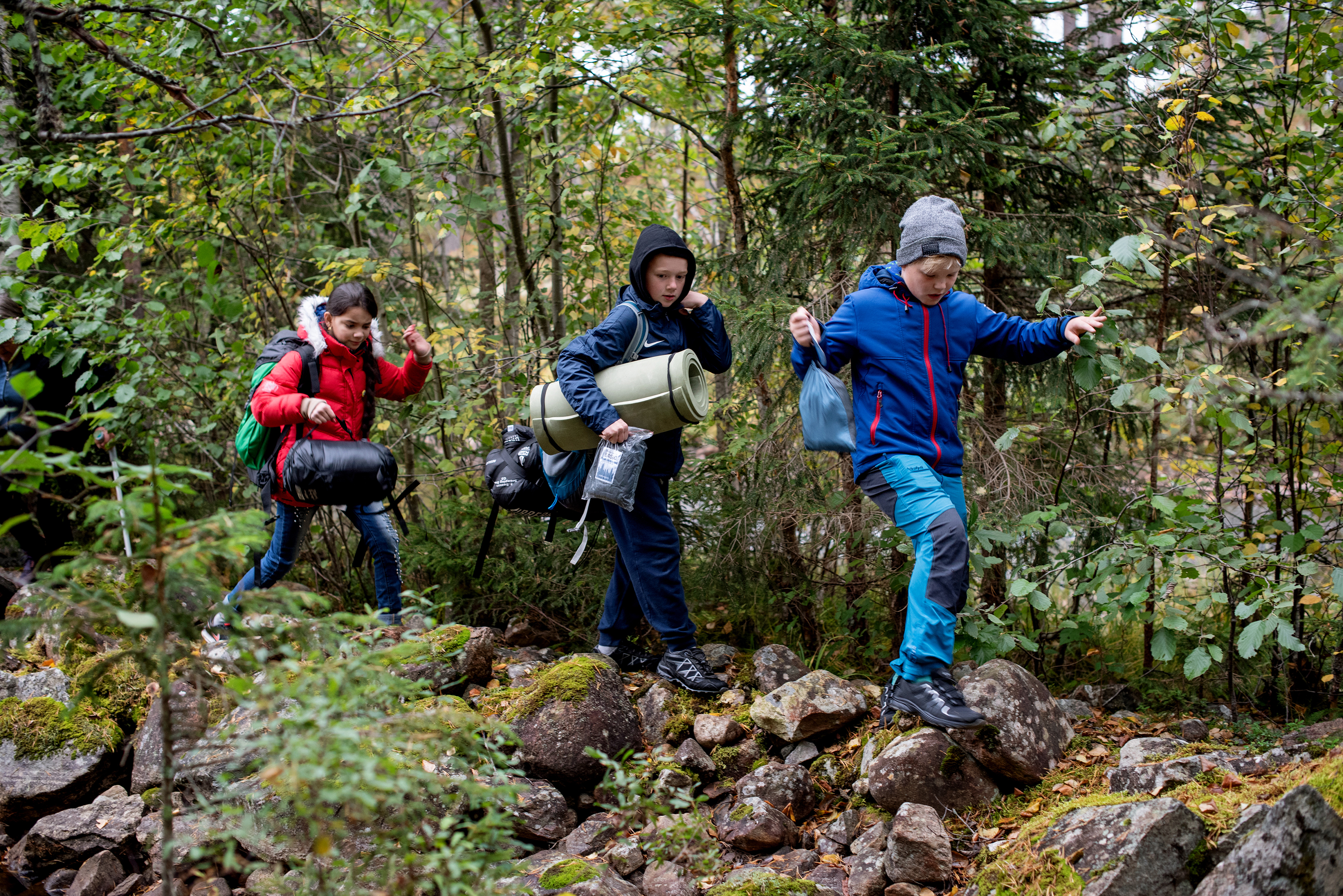 Lillian Solomon og Douua Ibrahim Al Ahmad er to av barne som koser seg i hengekøyene bildet t.v. Tre barn går på rekke og rad til leir stedet og bærer med seg utstyr Bildet t.h.