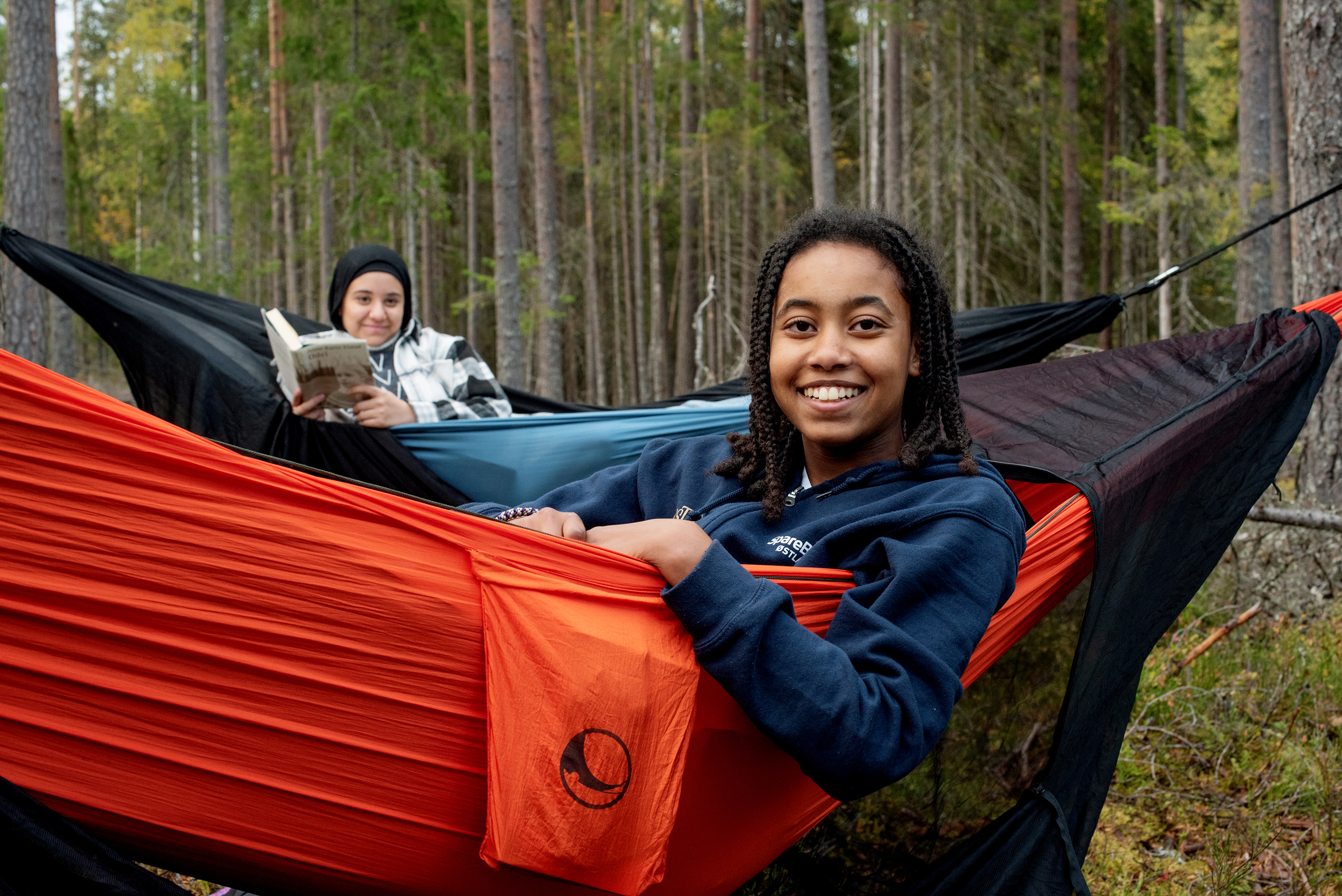 Lillian Solomon og Douua Ibrahim Al Ahmad er to av barne som koser seg i hengekøyene bildet t.v. Tre barn går på rekke og rad til leir stedet og bærer med seg utstyr Bildet t.h.