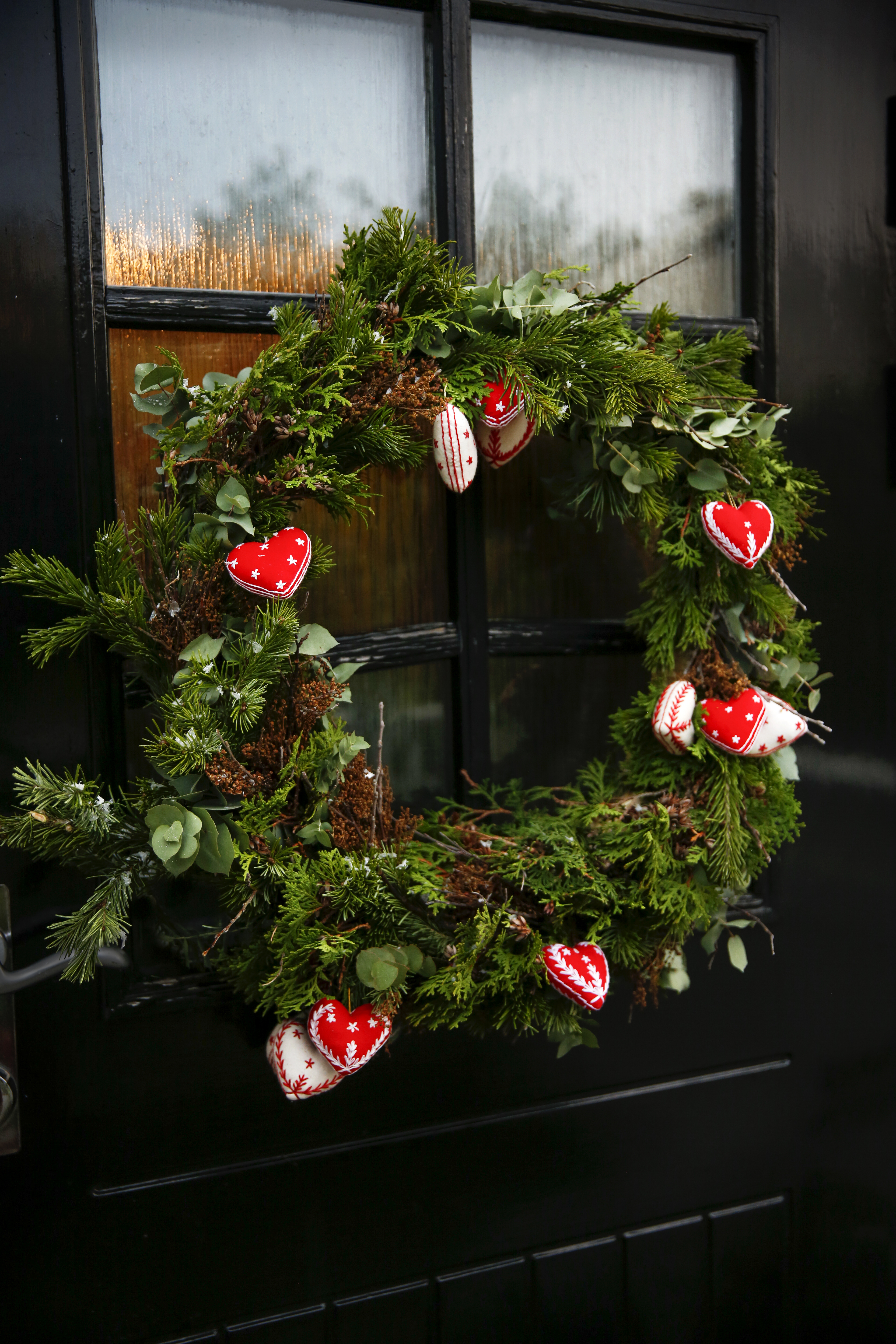 Pyntet julekrans med håndbroderte hjerter og en dame som syr.