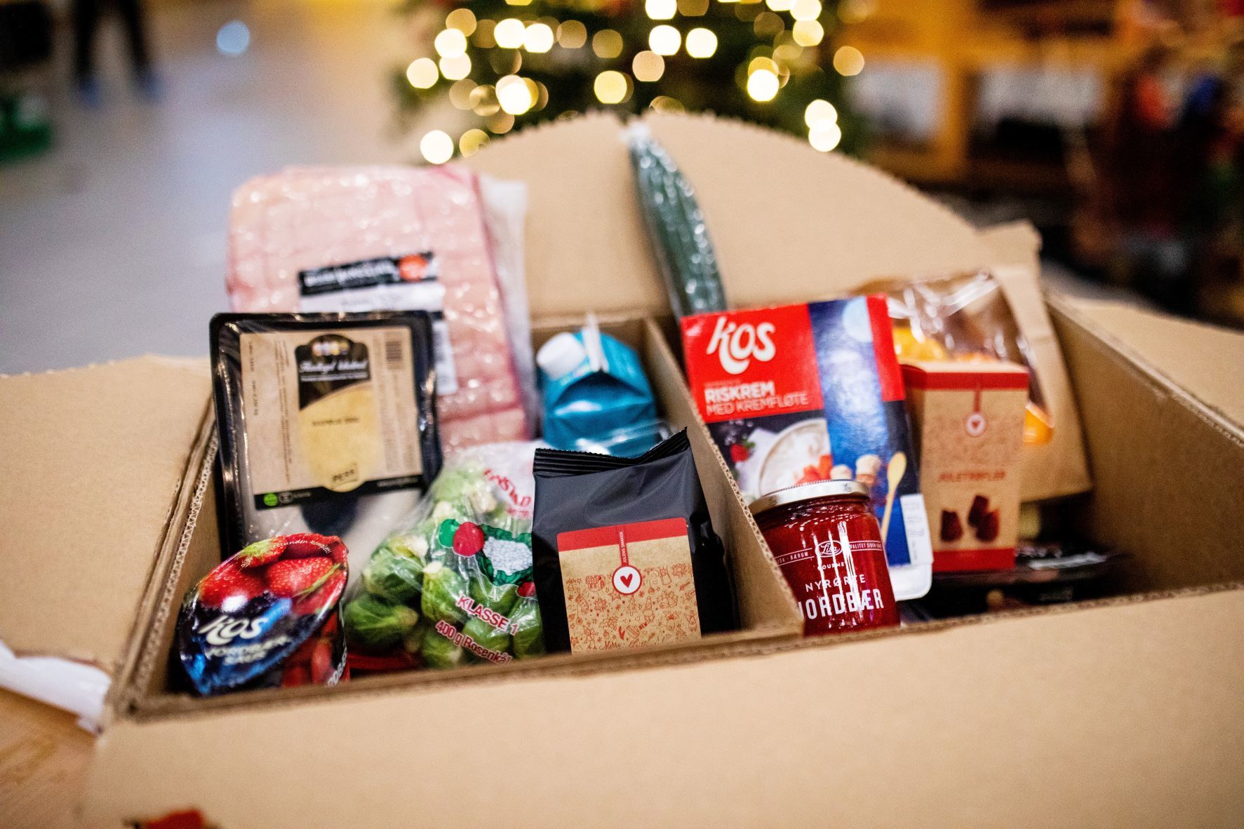 Person som bærer to bæreposer fulle med mat. Anonym, man ser kun fra livet og ned. En kasse med diverse mat.